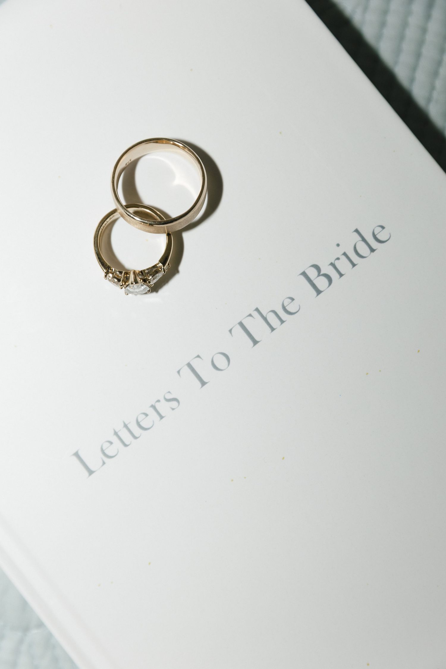A delicate gold engagement ring with diamonds sits elegantly next to a white letter or card on a light surface.