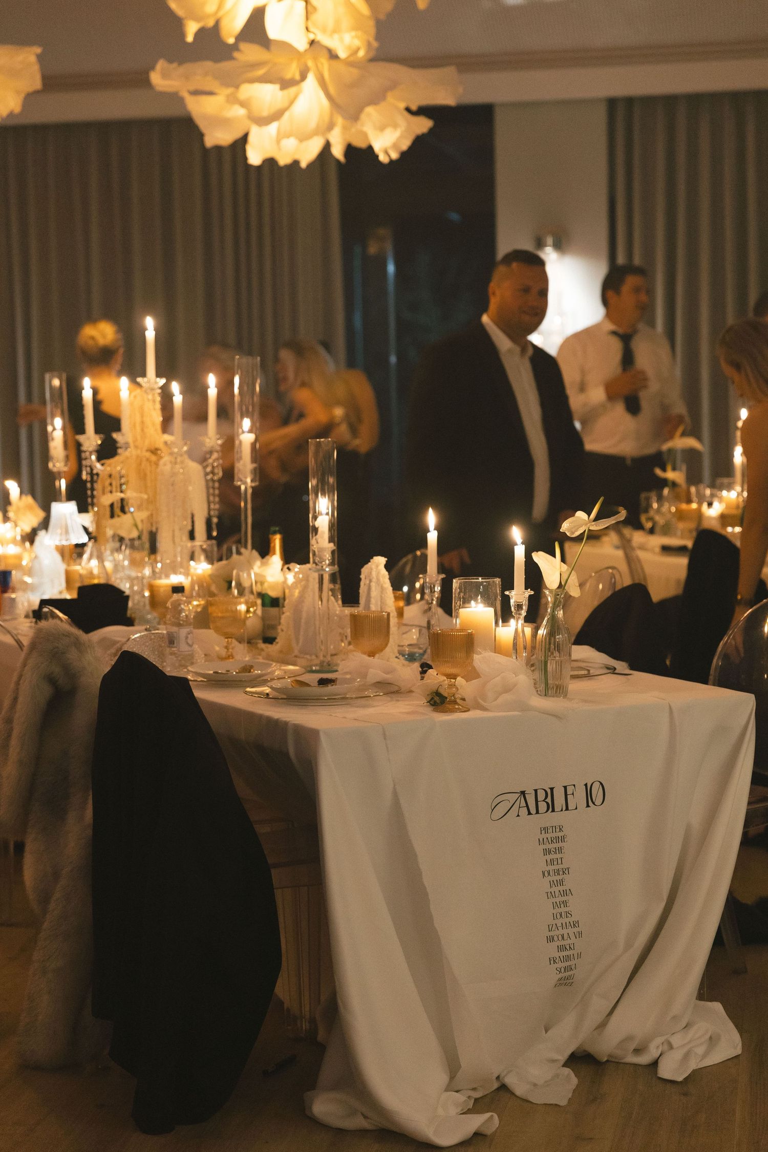 Elegant wedding reception tables with white linens, glowing candles and floral centerpieces in a dimly lit ballroom.