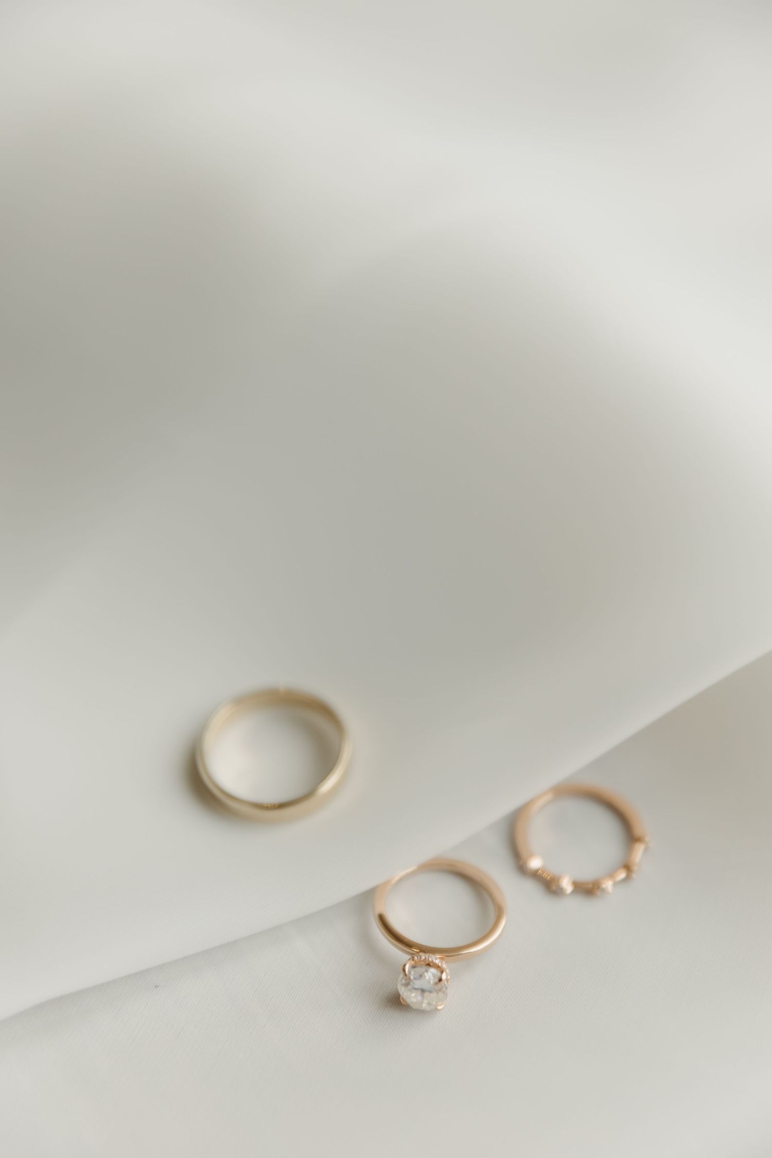 Gold wedding band and diamond hoop earrings on white fabric background, elegant bridal jewelry set.