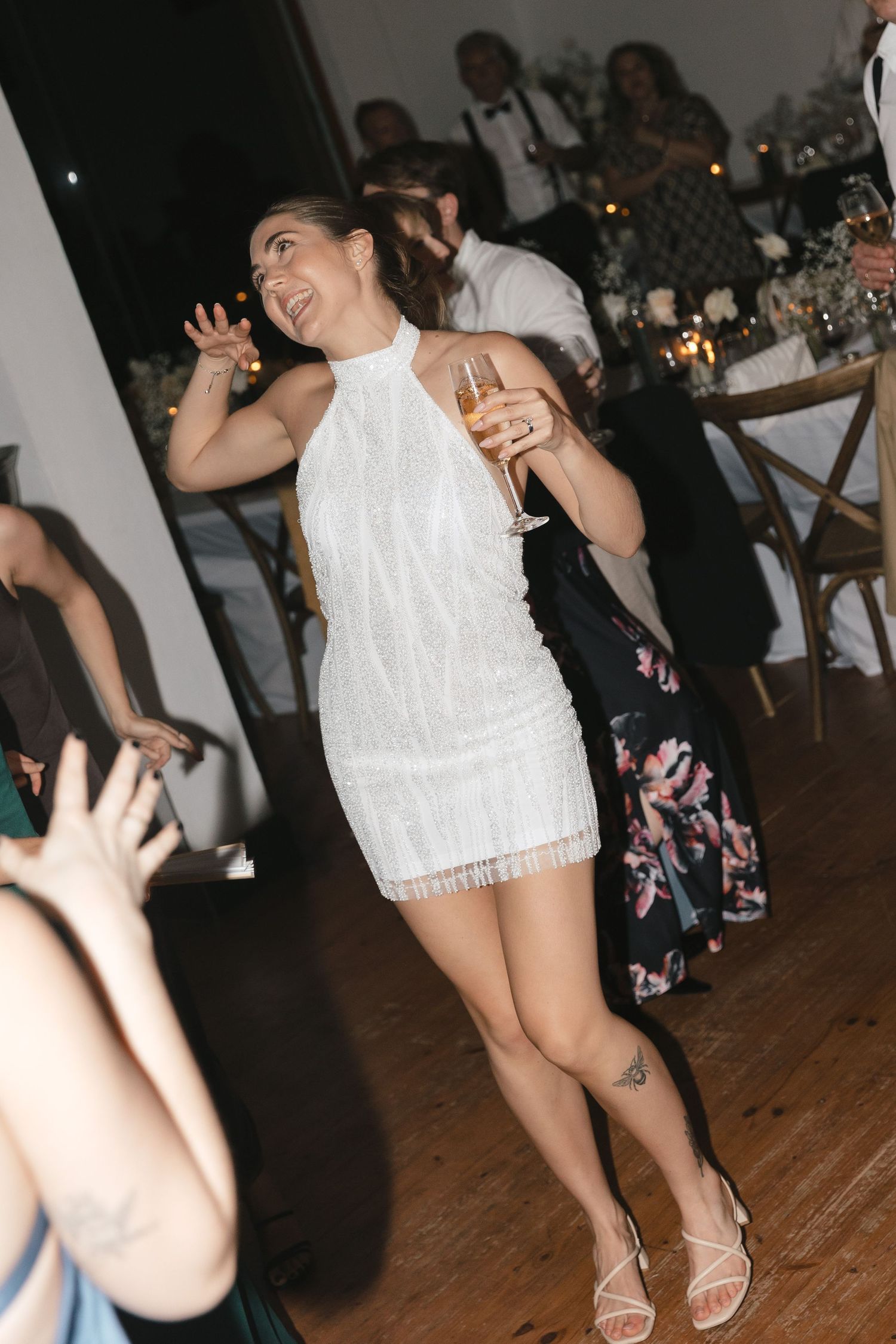 People dancing and celebrating at a wedding reception on a wooden dance floor in a dimly lit venue.