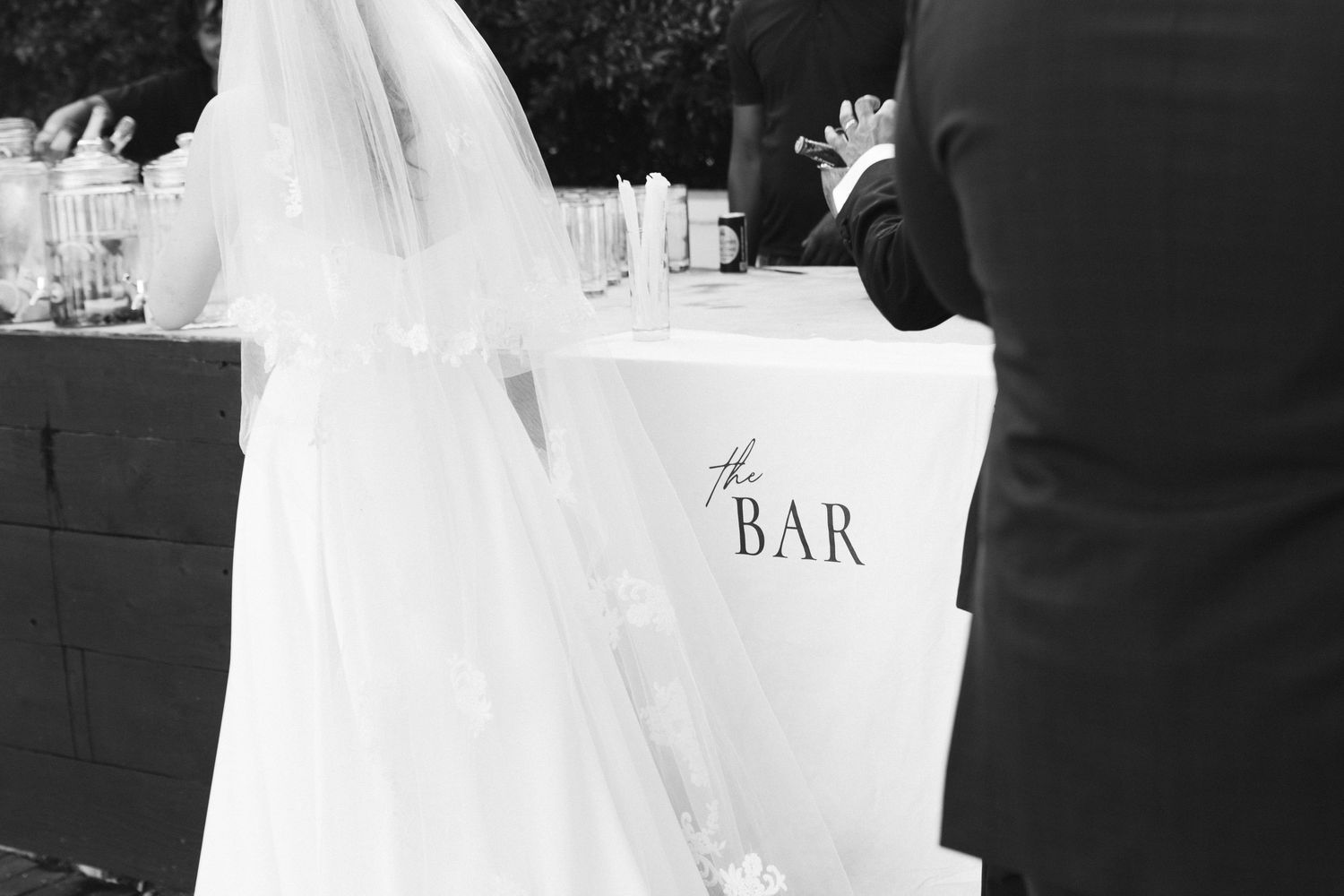 Elegant black and white wedding reception photo showing guests mingling near a bar area.