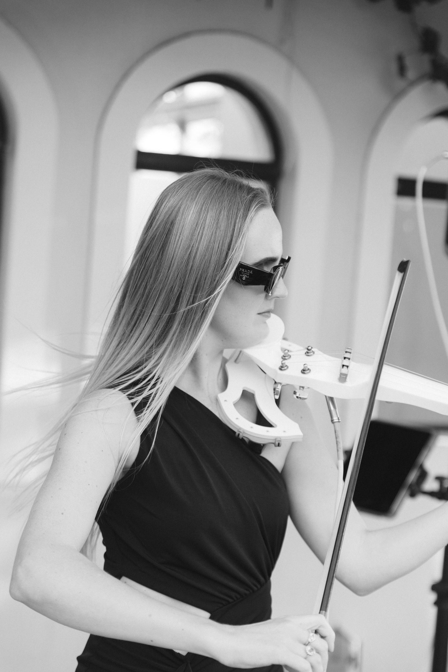Black and white photo of a violinist in sunglasses and sleeveless dress holding her instrument in an elegant pose.