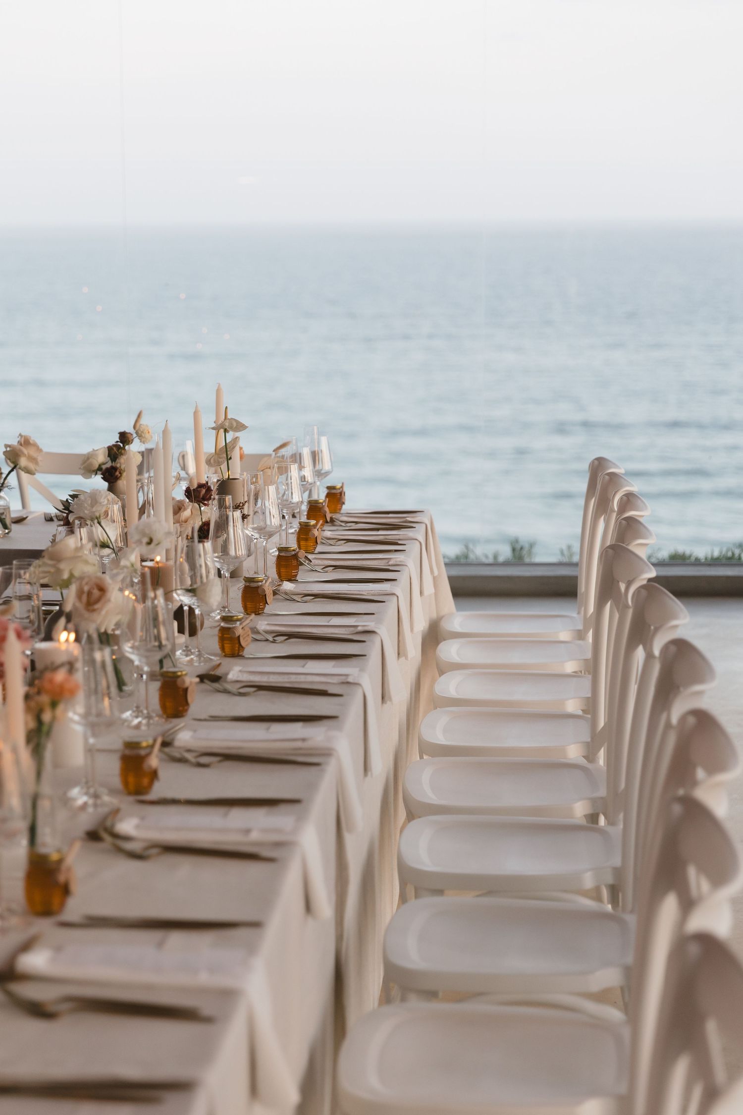 Elegant beachside dining table setup with white chairs and place settings overlooking the ocean horizon.