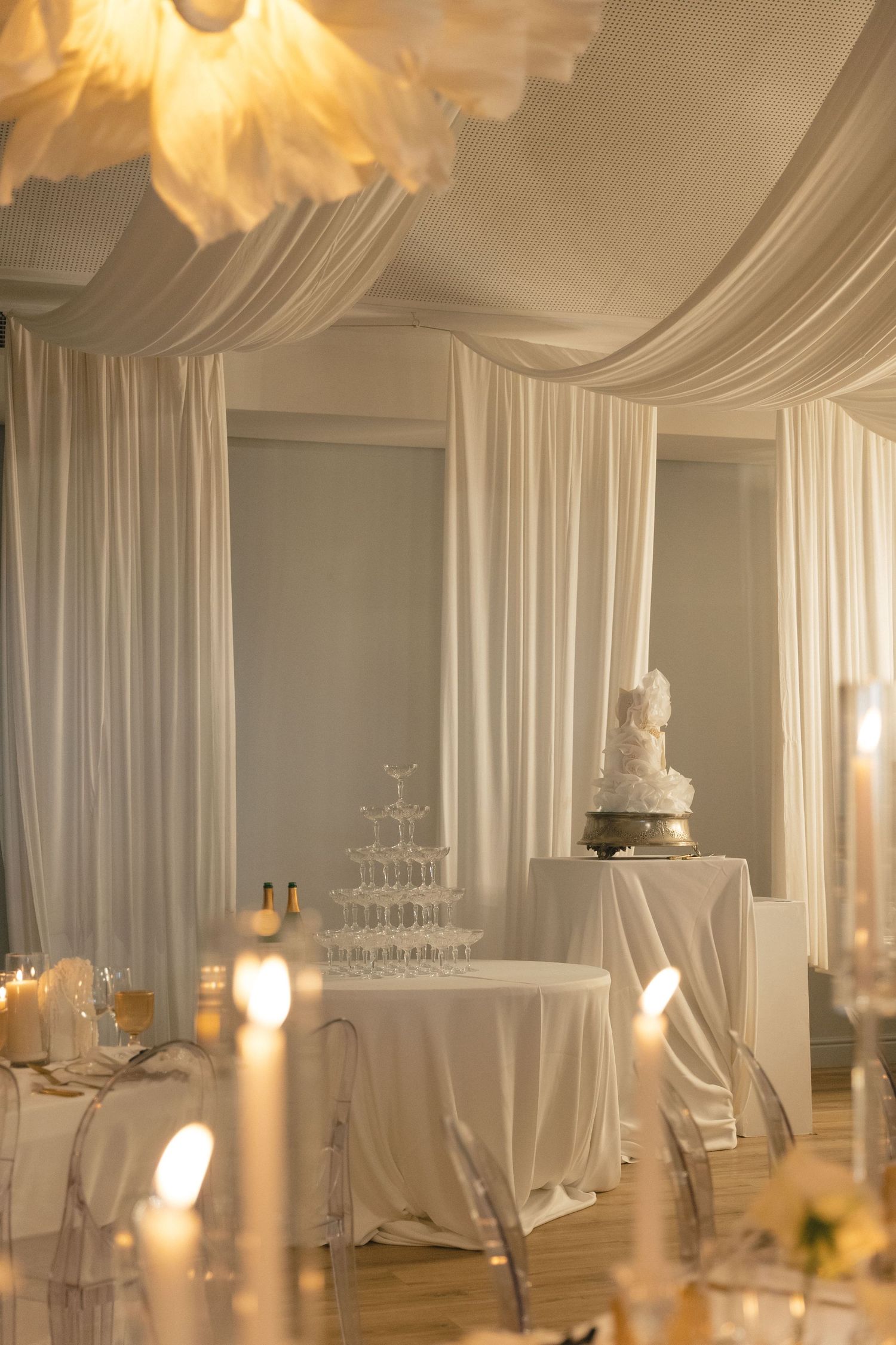 Elegant white wedding reception venue with draped fabric ceiling and soft lighting.
