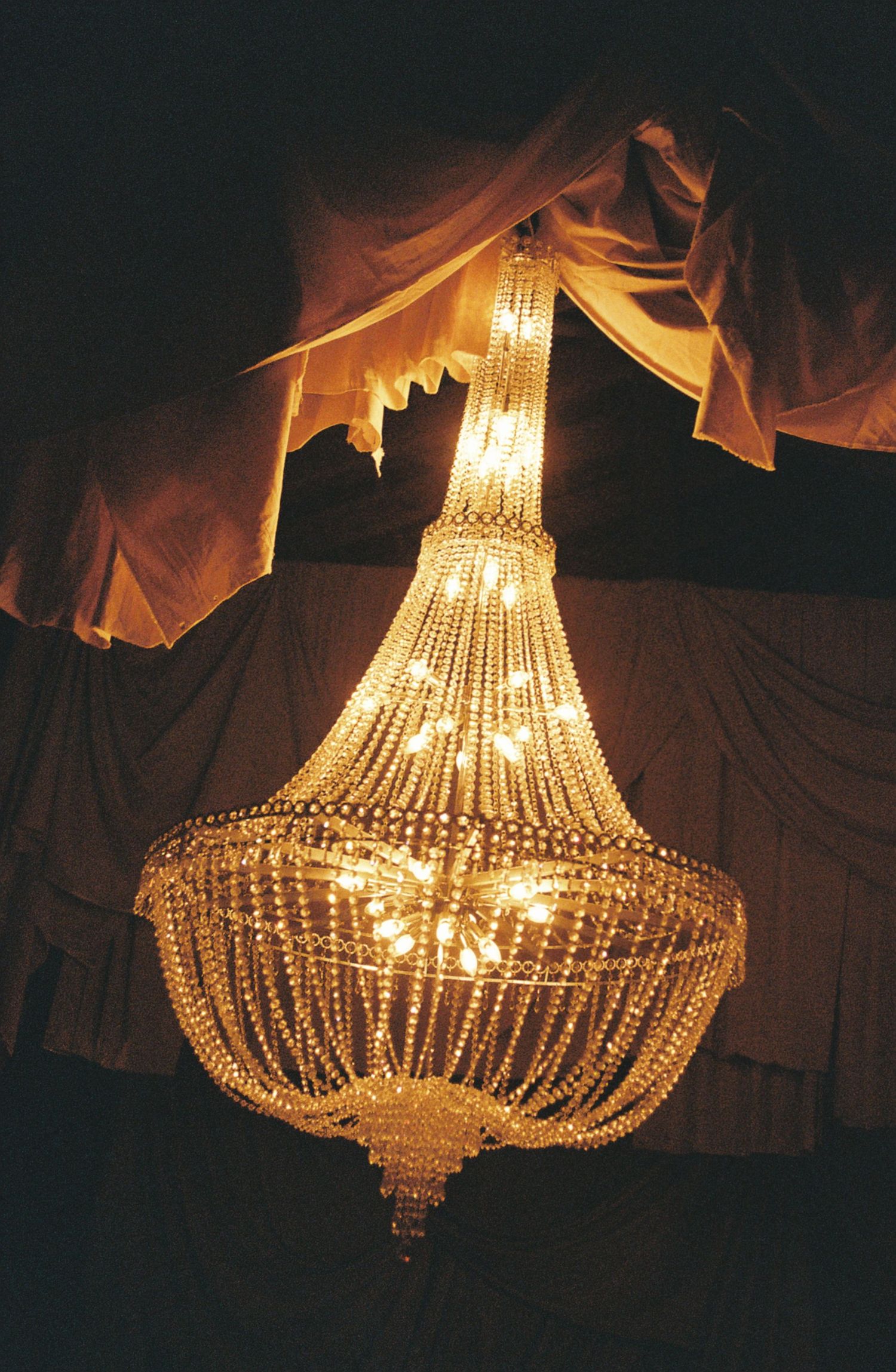 Ornate crystal chandelier glows warmly against dark background, creating a luxurious ambiance.
