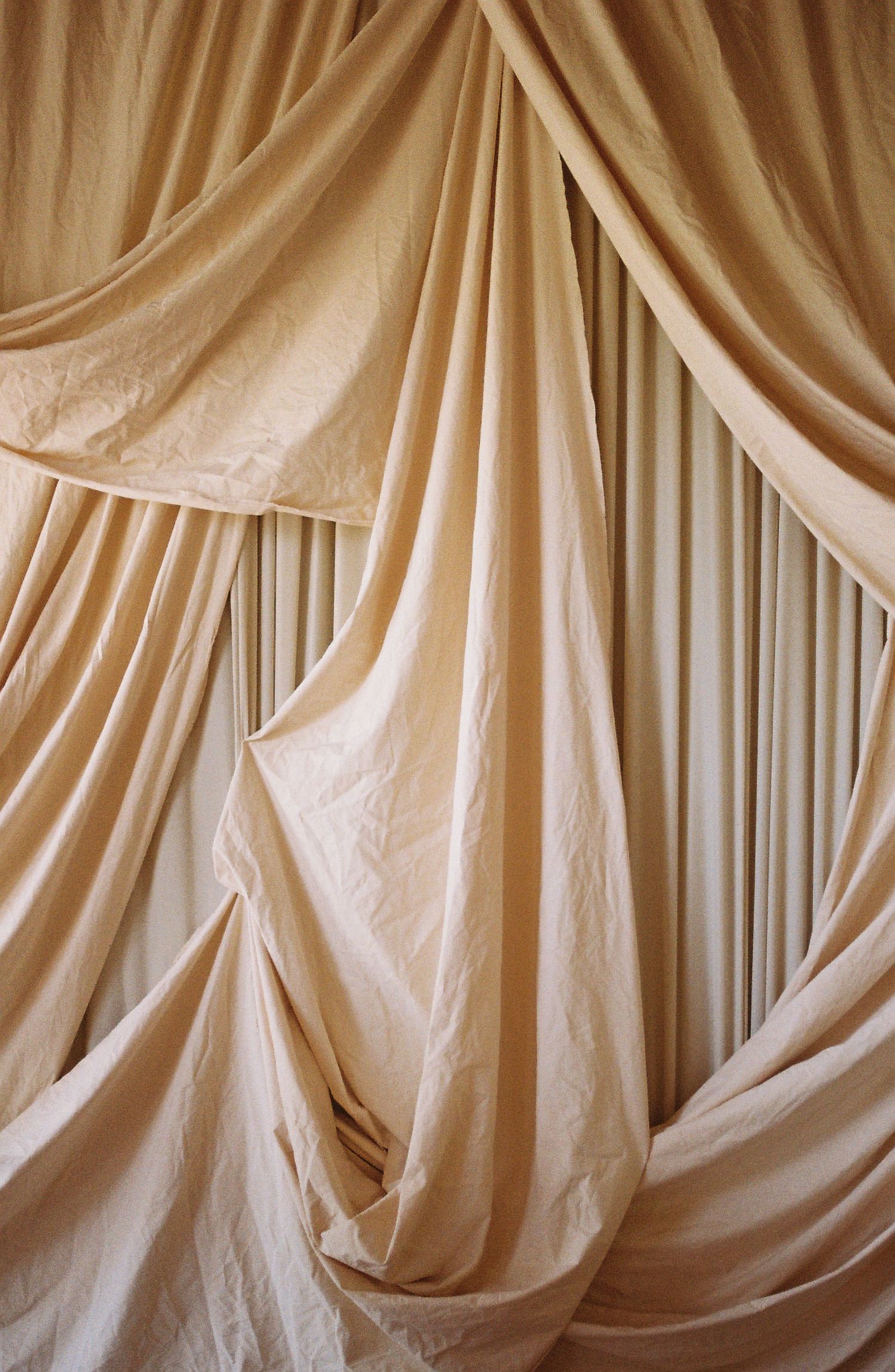 Elegant cream-colored fabric drapes create a soft, flowing backdrop with graceful folds and curves.