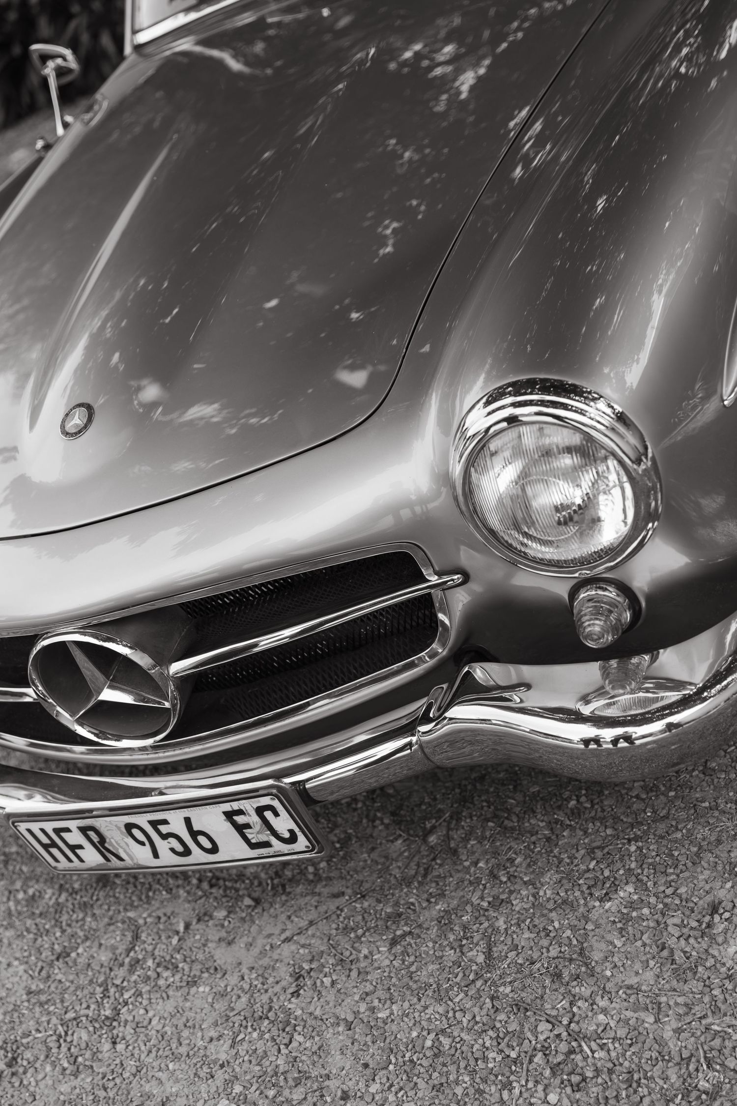 Black and white photo of a classic Mercedes-Benz vintage car front view with chrome headlight and grille detail.