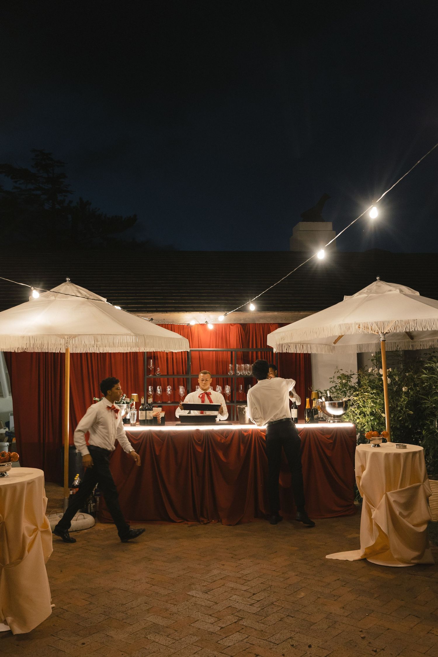 Outdoor evening wedding reception setup with white tents and string lights illuminating buffet tables at dusk.