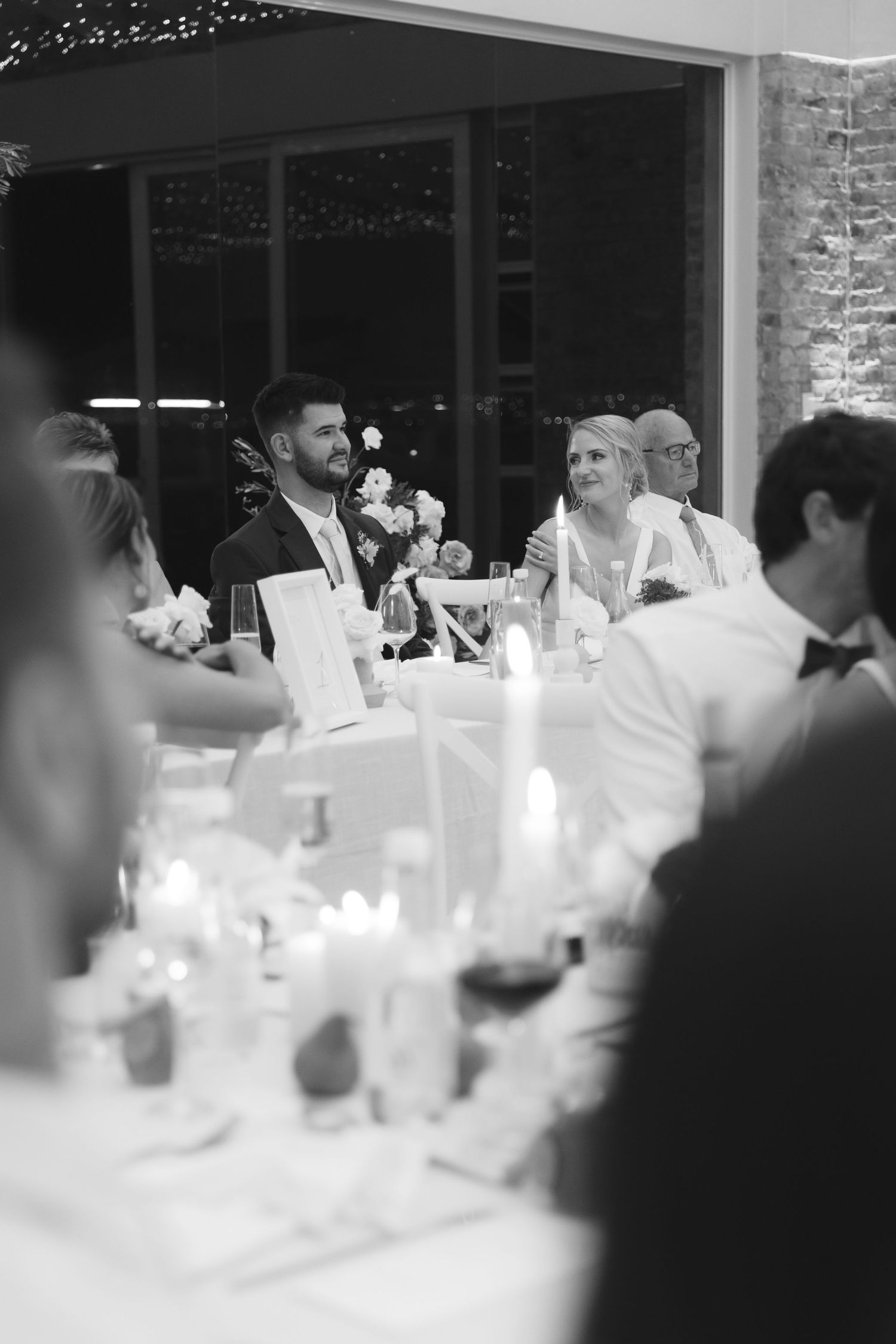 Wedding reception guests seated at elegant white-clothed tables with glowing lights creating an intimate atmosphere.