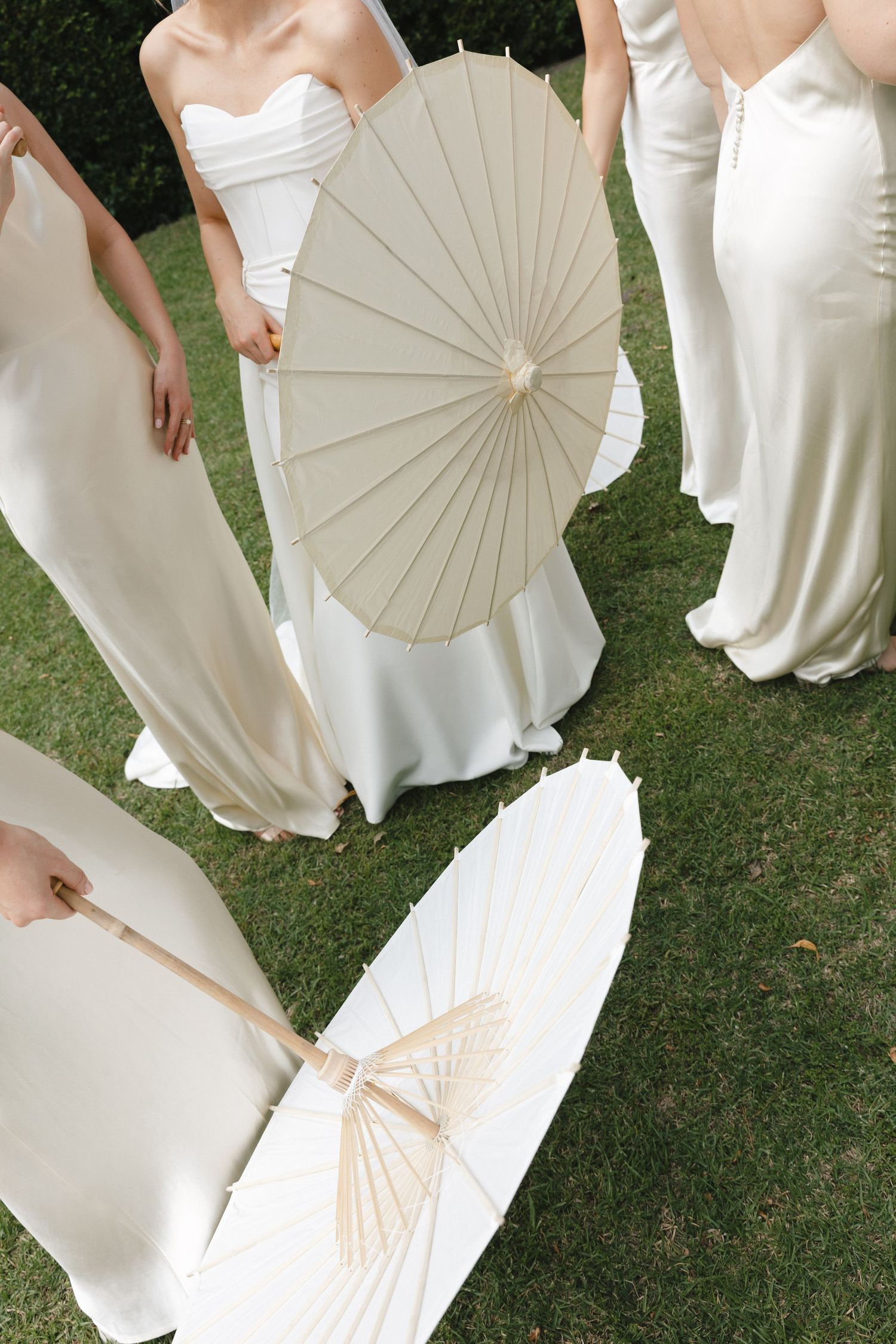 A group in white dresses holds delicate paper parasols while standing on grass during an outdoor event.
