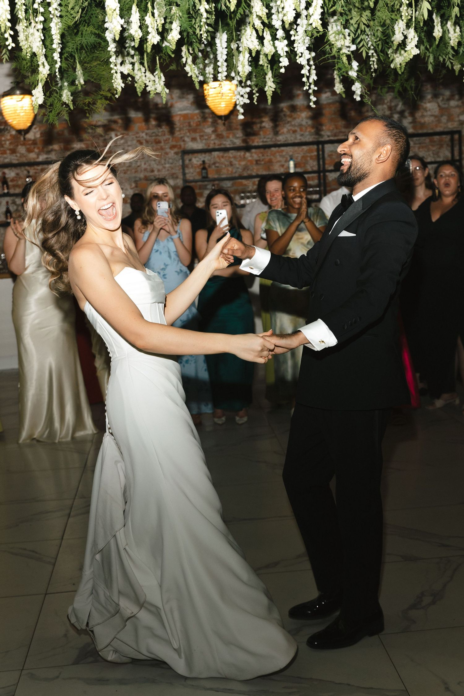 A couple performs a romantic dip during their first dance at a wedding reception under hanging floral decorations.