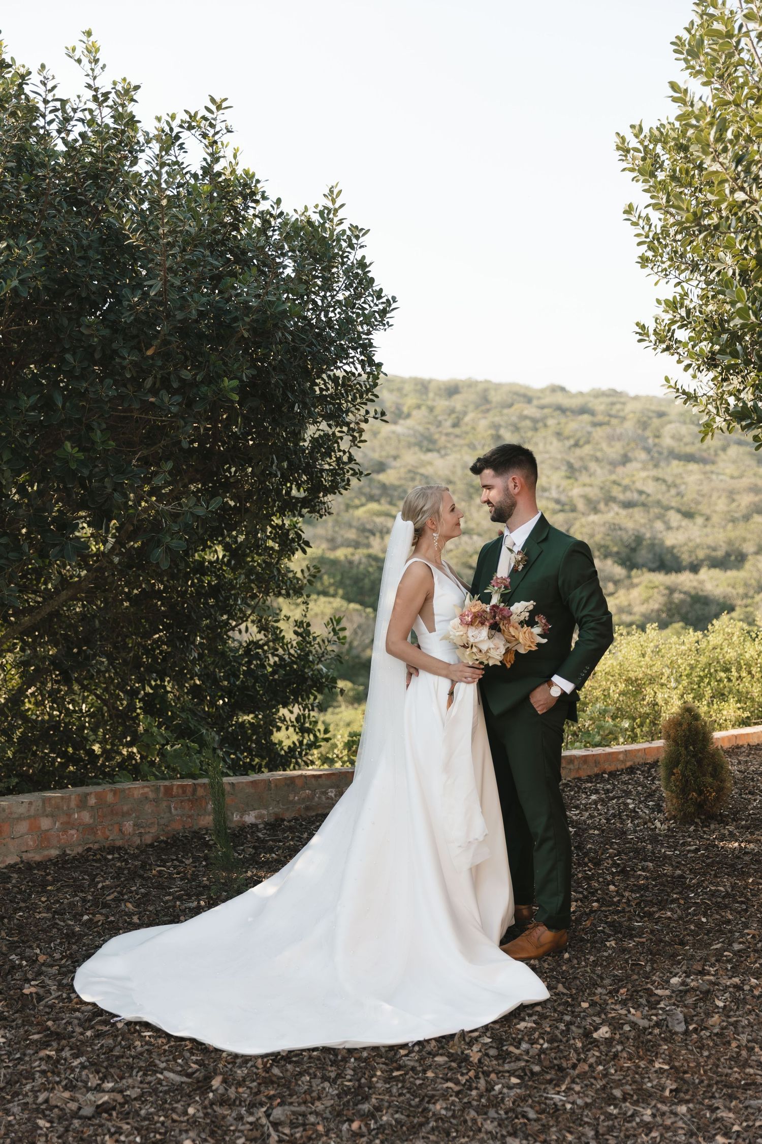 A couple shares a romantic moment on a hillside surrounded by trees during their wedding photoshoot.