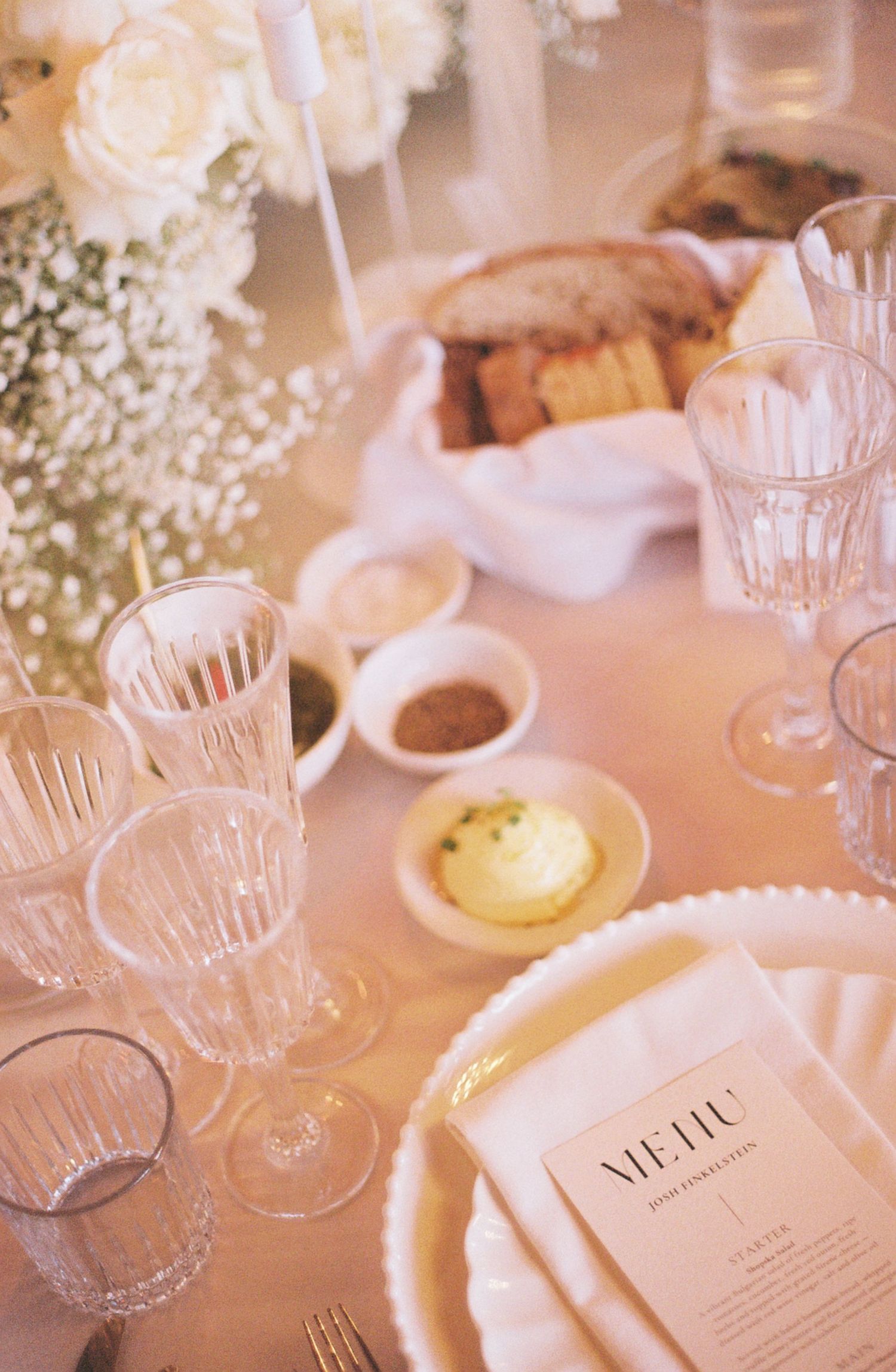 Elegant table setting with crystal glasses, menu cards, and white roses in a soft pink-tinted romantic atmosphere.