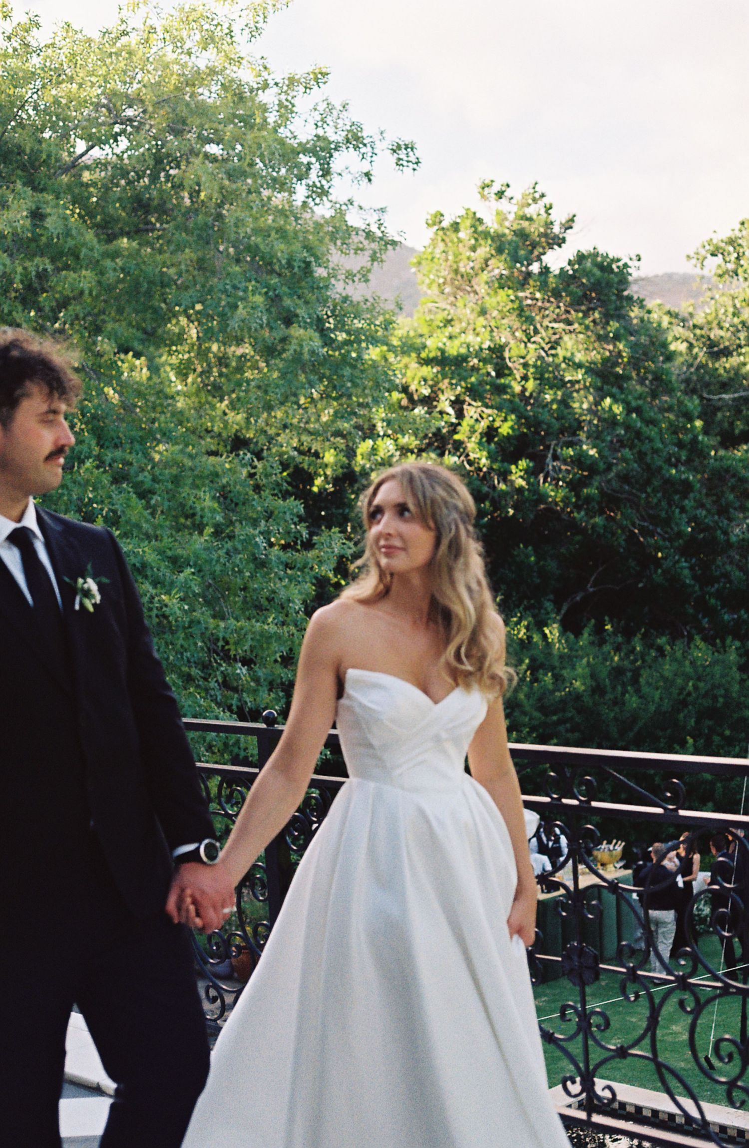 Elegant outdoor wedding reception on a balcony with ornate black railings and greenery backdrop.
