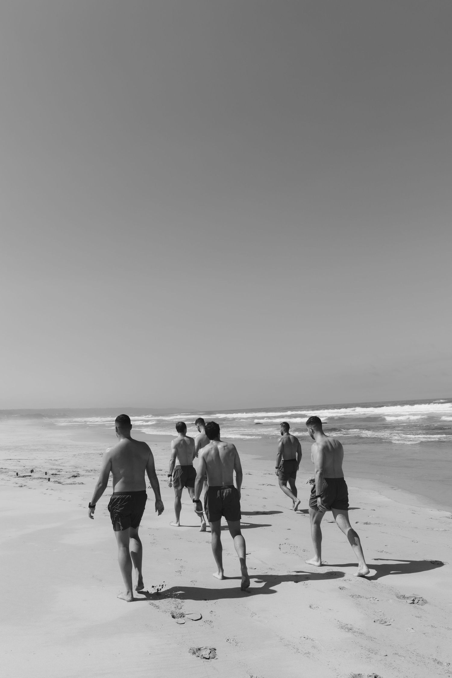 A group of people walking along a beach shoreline in black and white vintage photography.