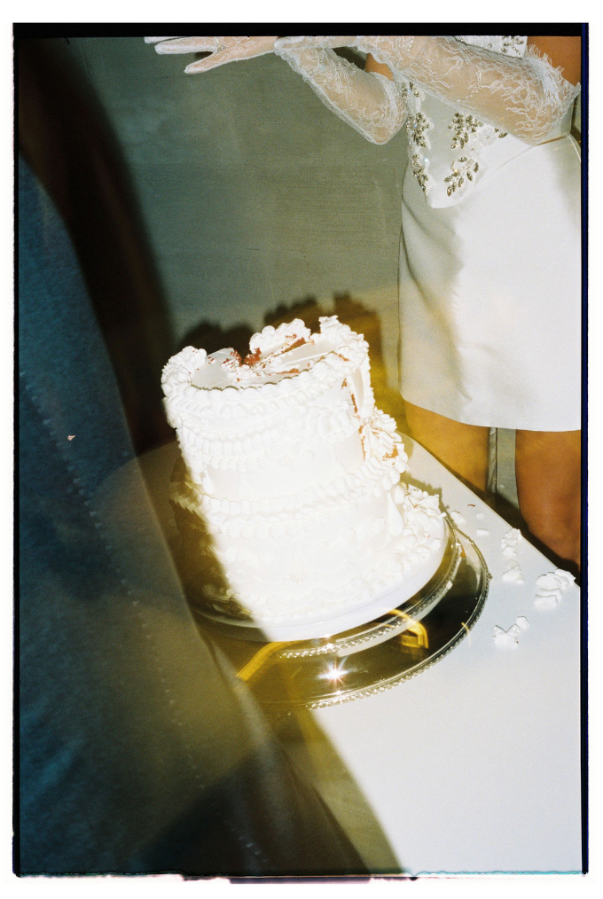A vintage-style photograph shows a white wedding cake with frosting details against a blurred background.