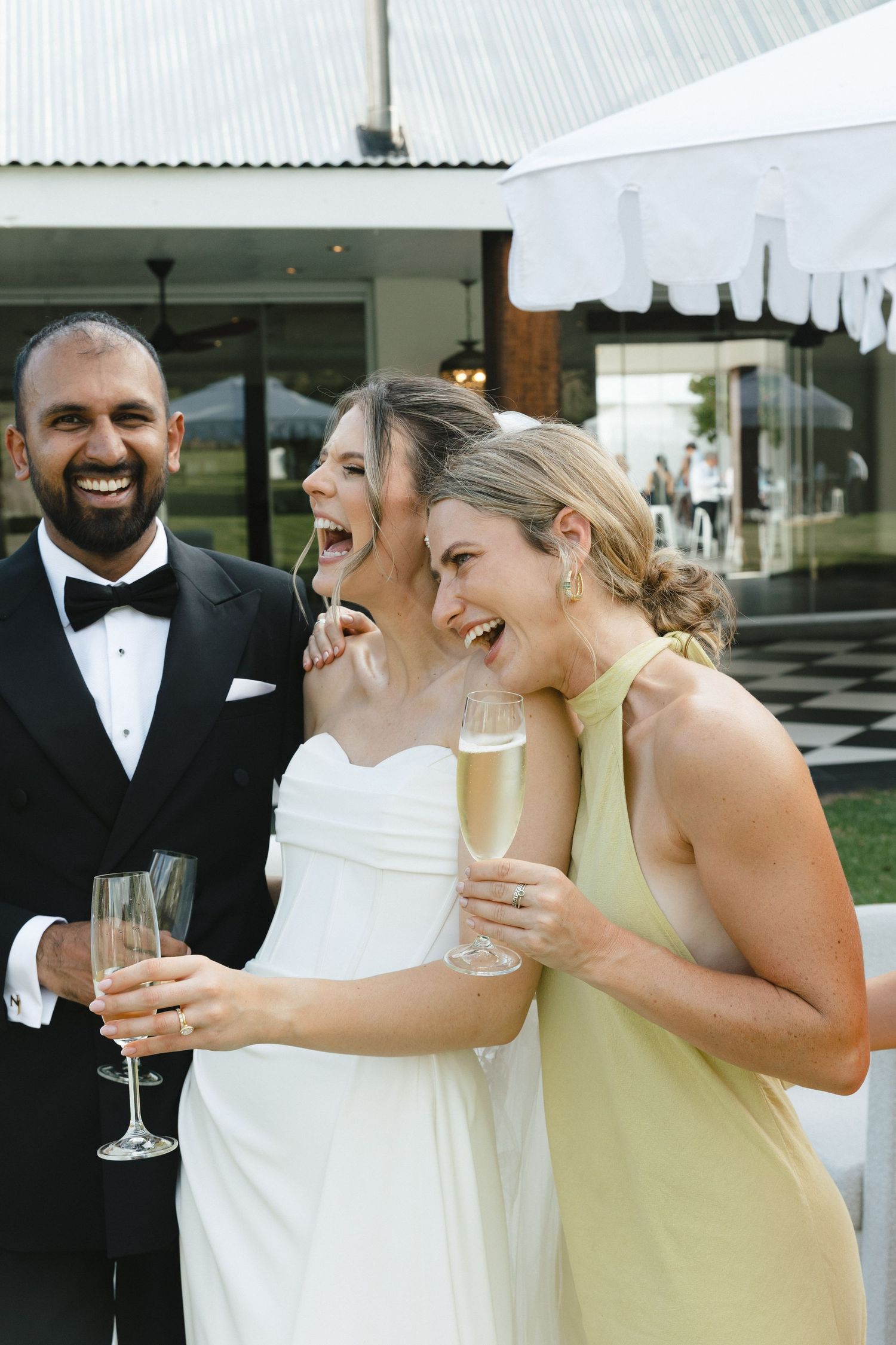 Wedding party members laugh and share champagne together during celebratory moment at outdoor reception.