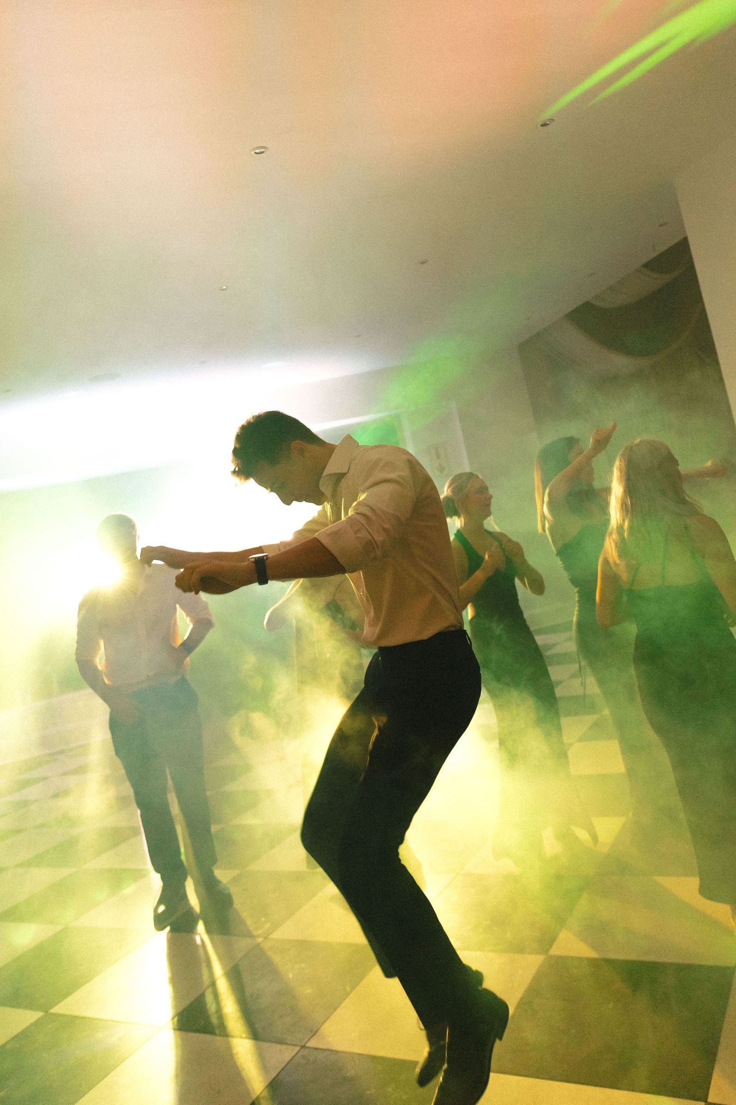 Dancers perform in a hazy nightclub with dramatic green lighting and smoke effects creating a dynamic party atmosphere.