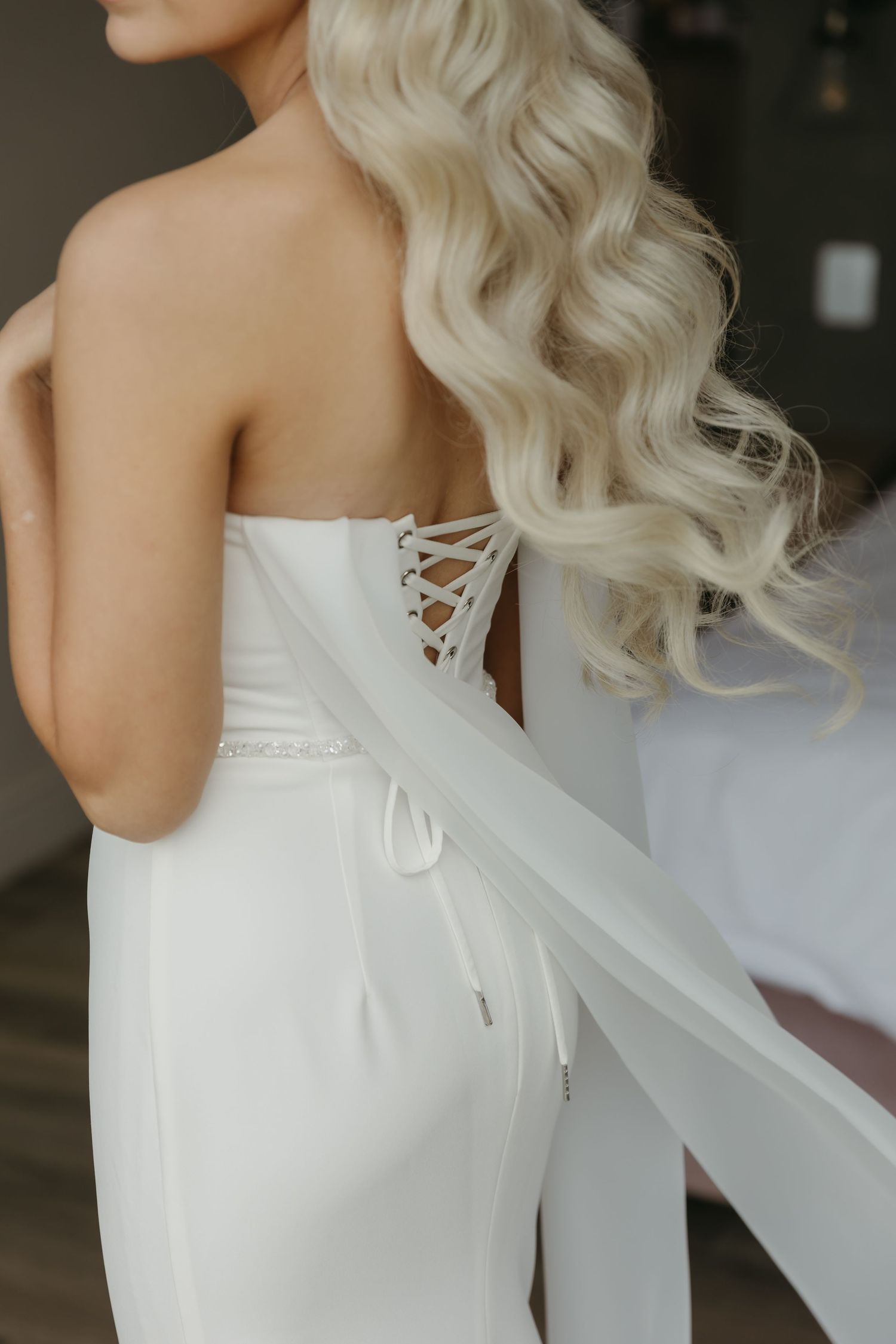 Close-up back view of bride in strapless white wedding gown with elegant lace-up corset detail and flowing veil.