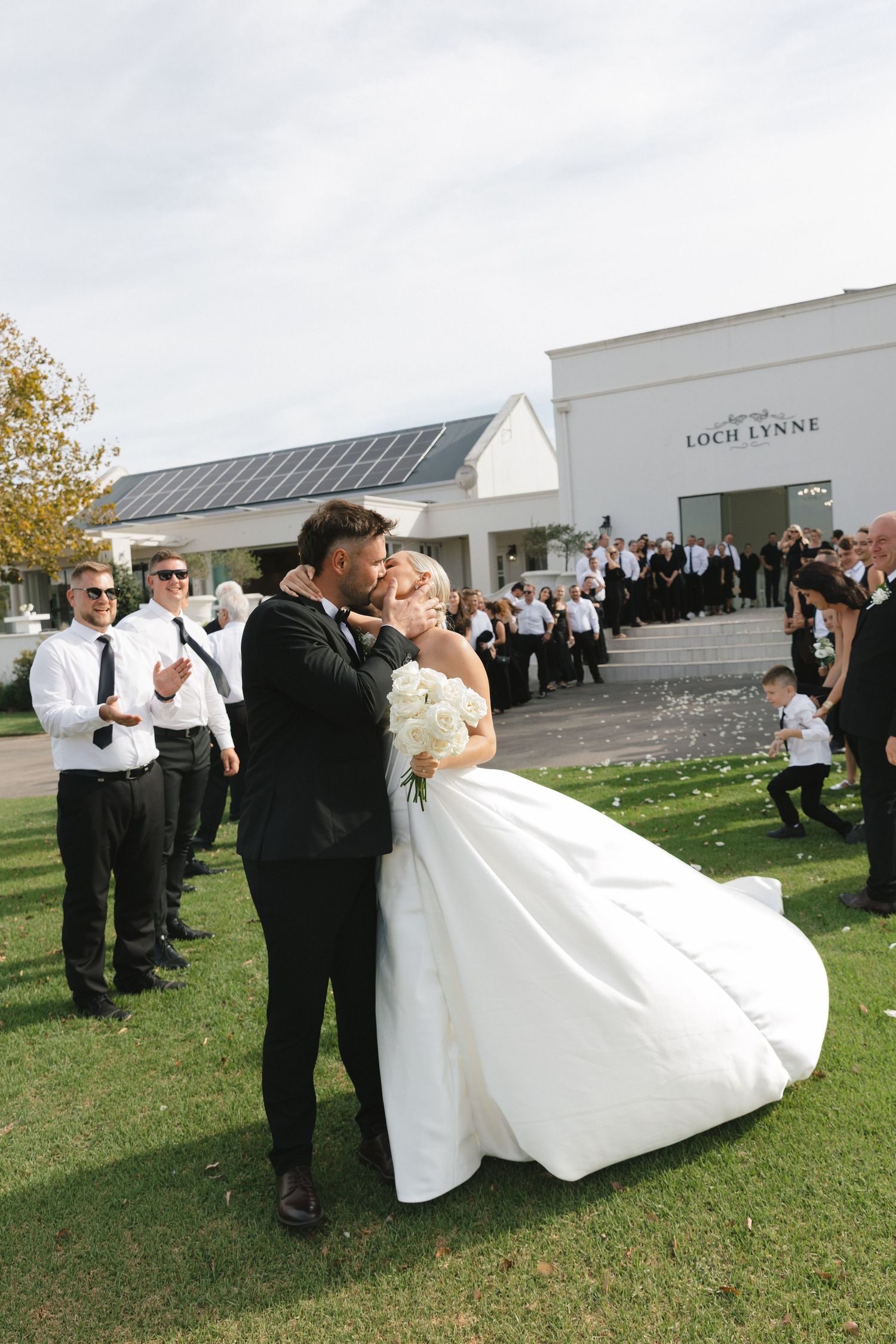 A series of wedding photos showing the couple and wedding party celebrating on a grassy lawn outside a white building.