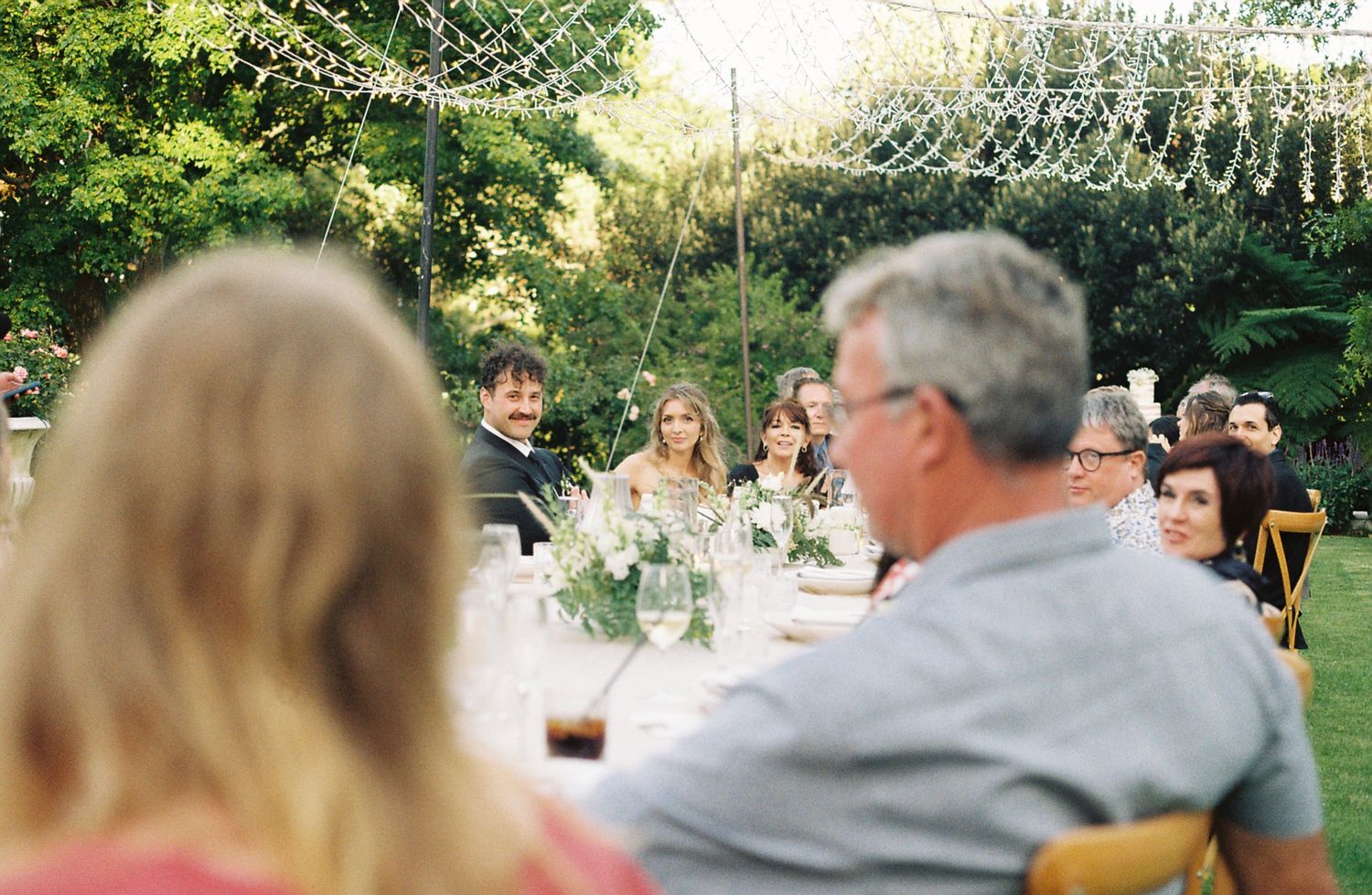 A group of people enjoying an outdoor wedding reception in a garden setting with tables and chairs.