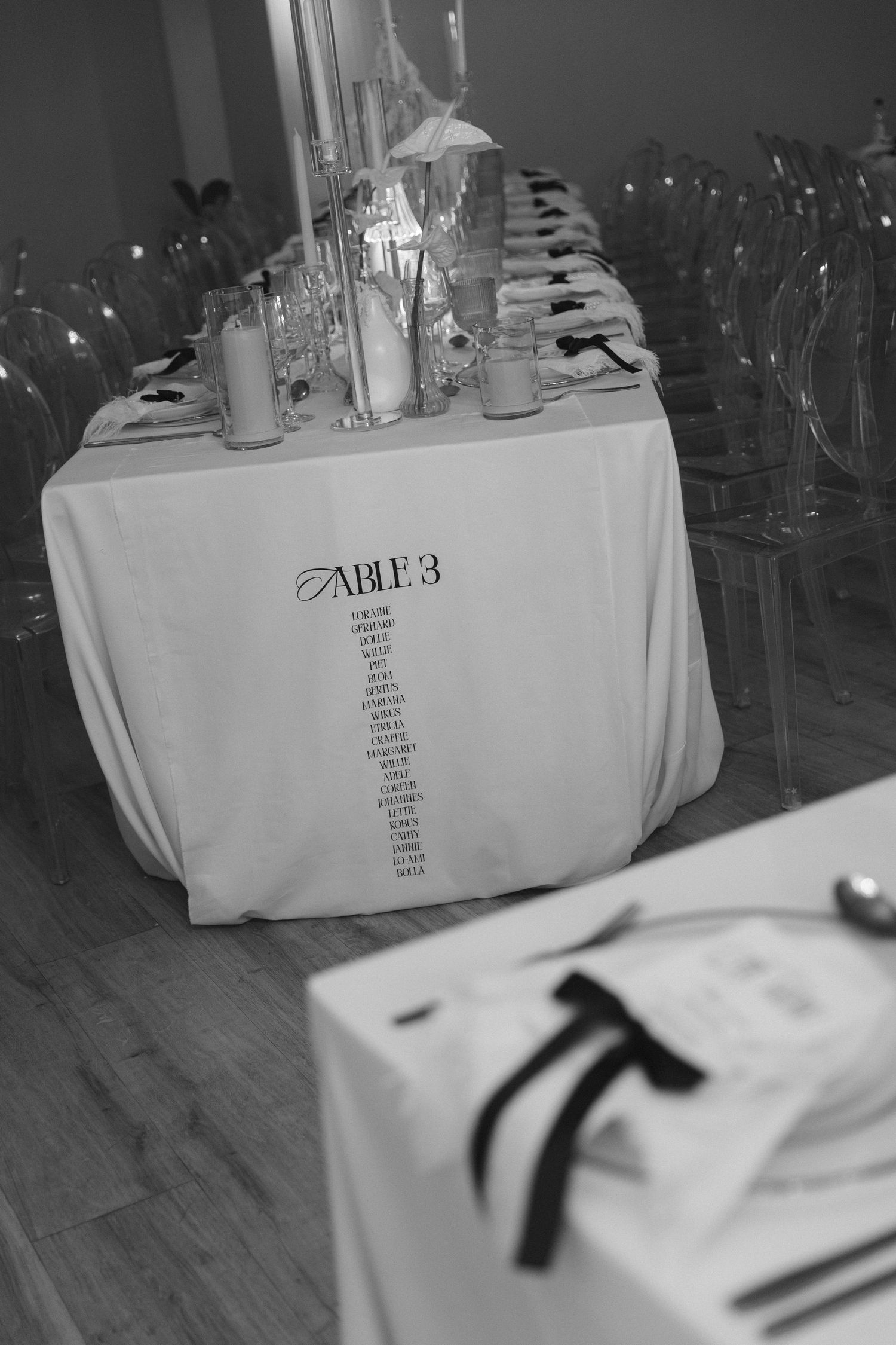 Black and white photo of elegant table settings with white tablecloths and glassware arranged in a row.