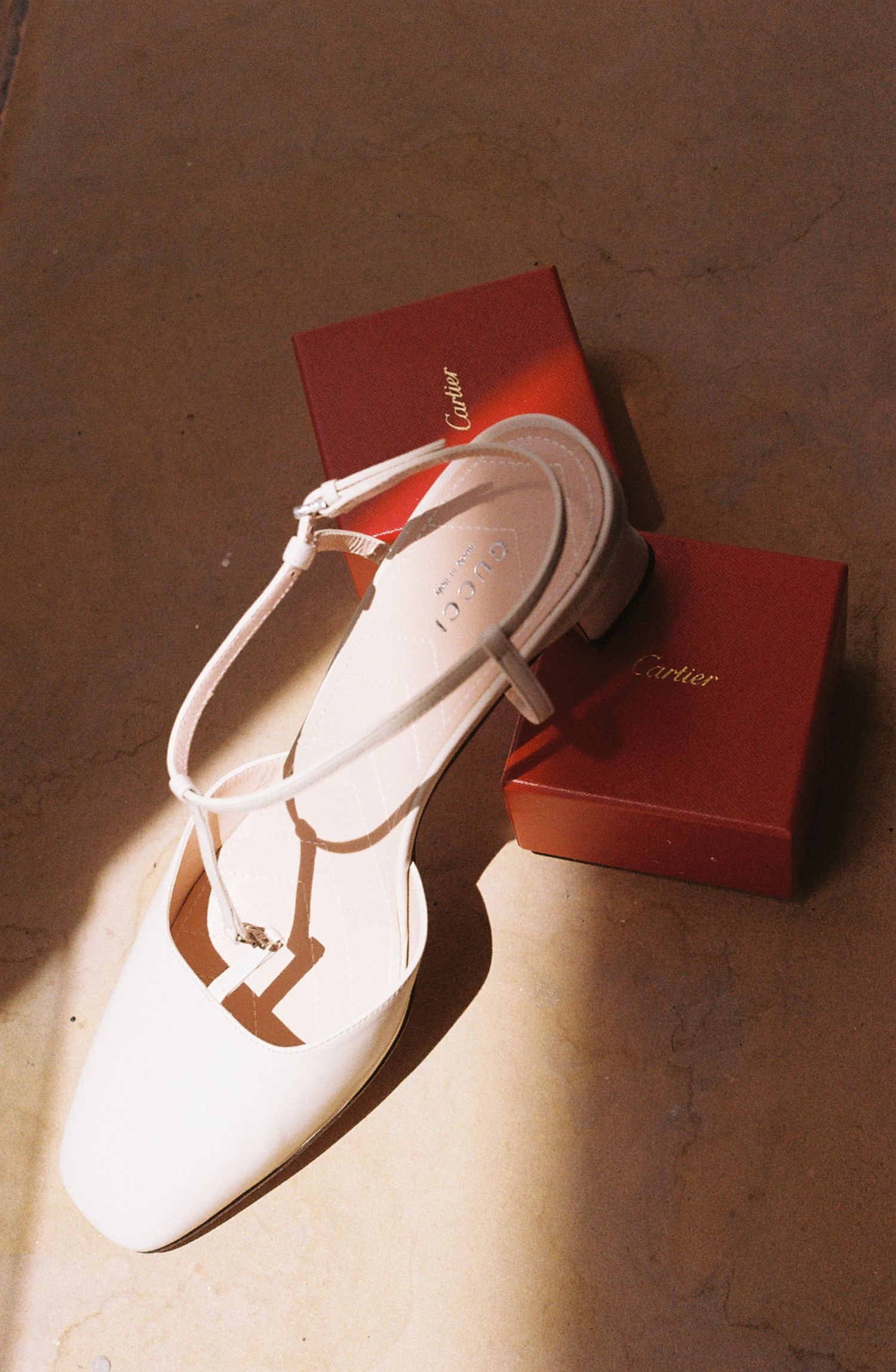 White flip-flop sandal with red box casting dramatic shadows on beige surface in artistic product photography series.