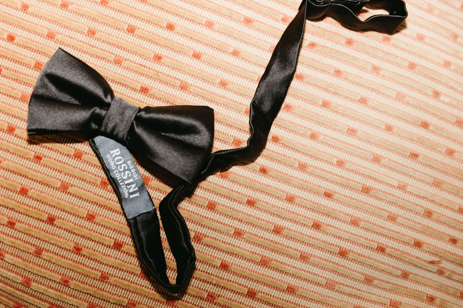 Black satin bow tie with label on orange dotted fabric background.