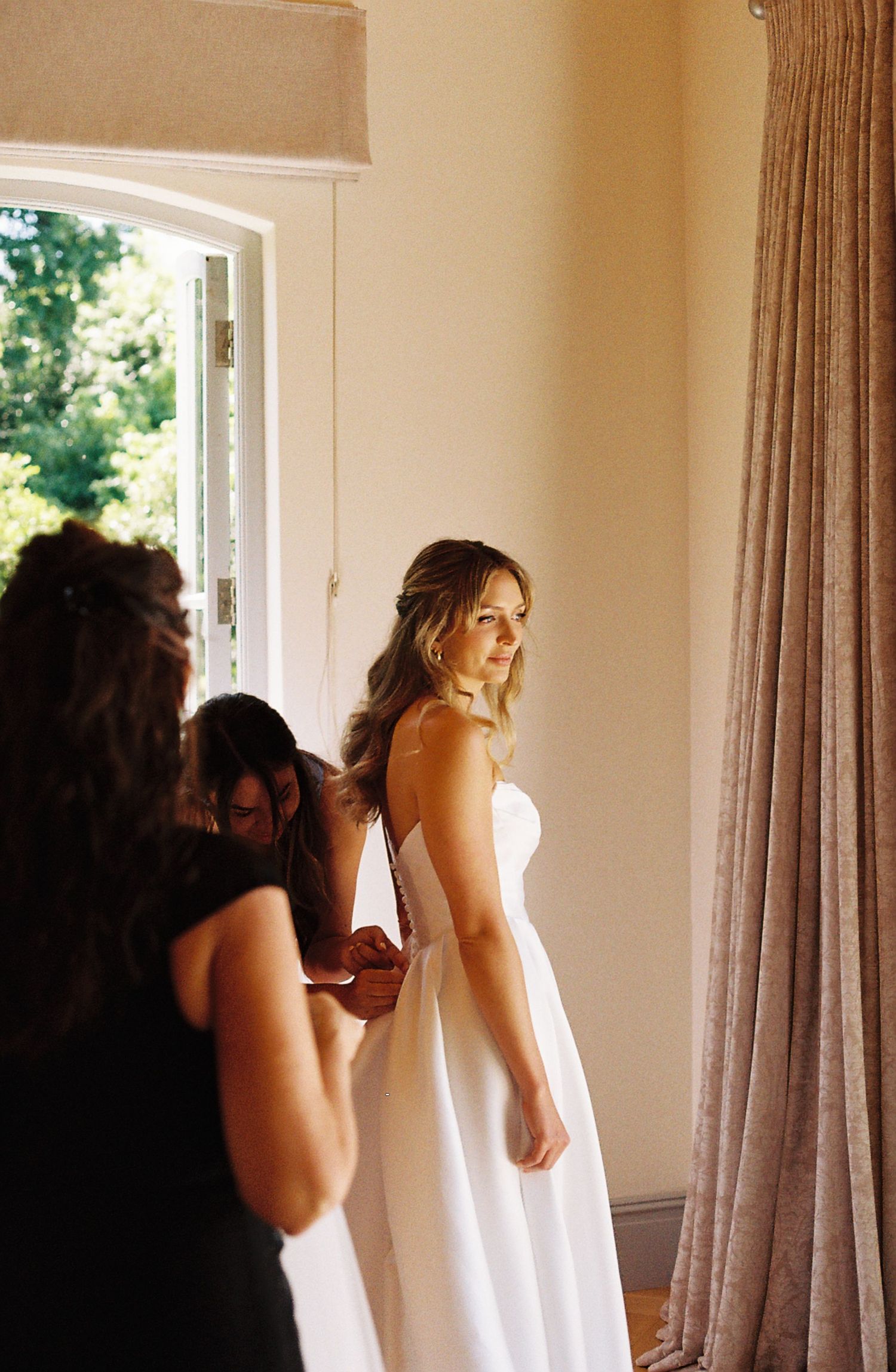 A series of five connected film photographs showing a person in a white dress being fitted near a window with natural light.
