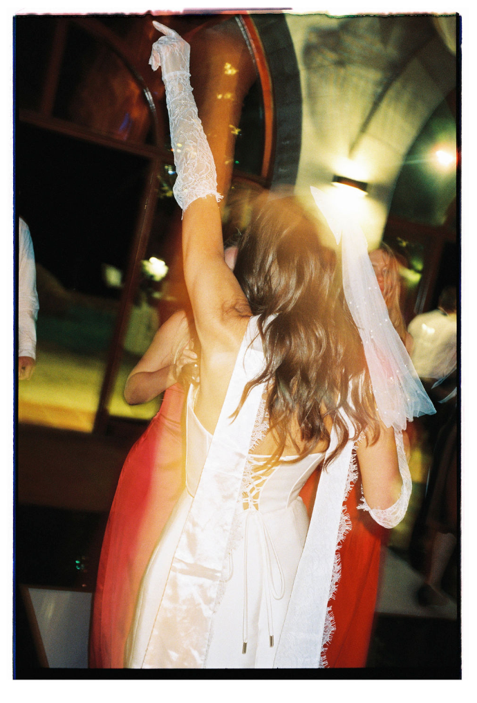 Blurry motion sequence of someone dancing in a white top and red pants under dim lighting at night.