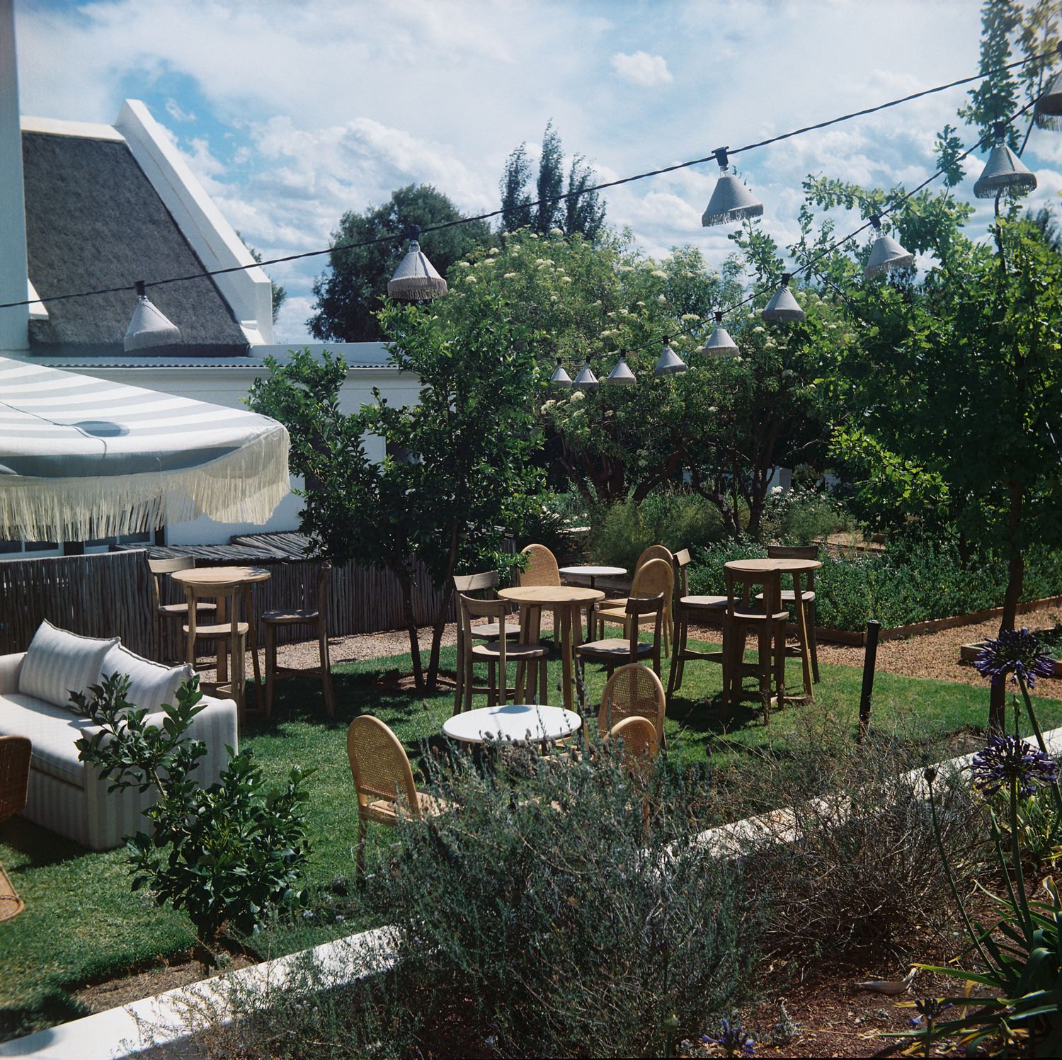 An outdoor wedding venue setup with wooden tables and chairs arranged on a grassy lawn under blue skies.