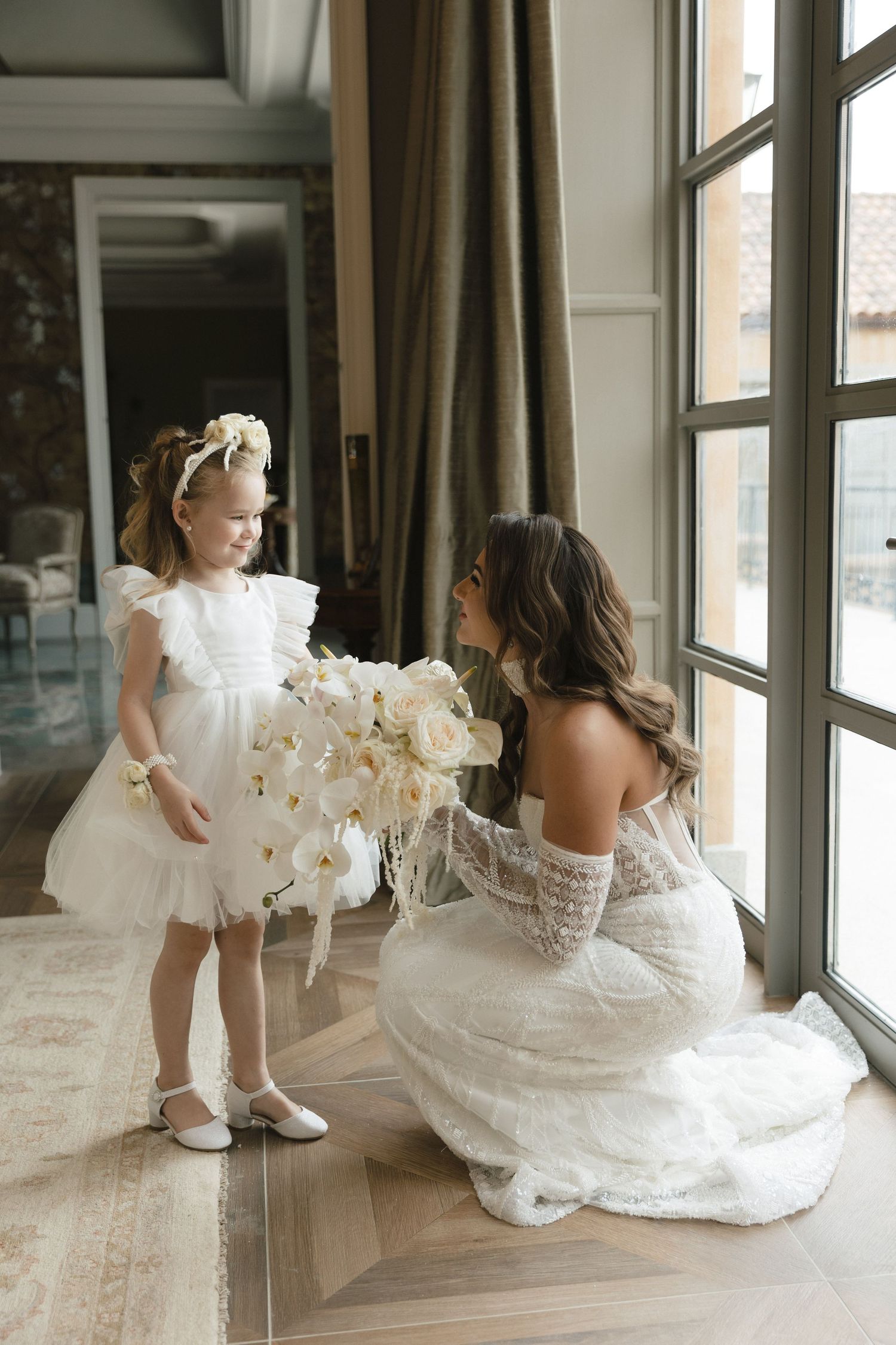Elegant white wedding gowns photographed near large windows with natural light streaming in.