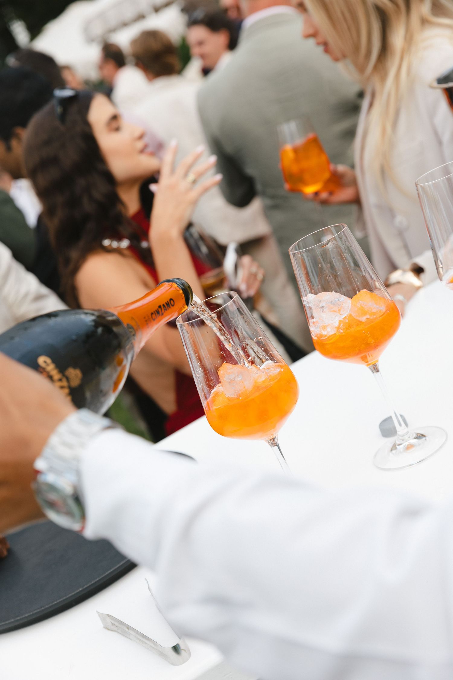 Orange cocktails in stemmed glasses sit on white tablecloths at an elegant party gathering.