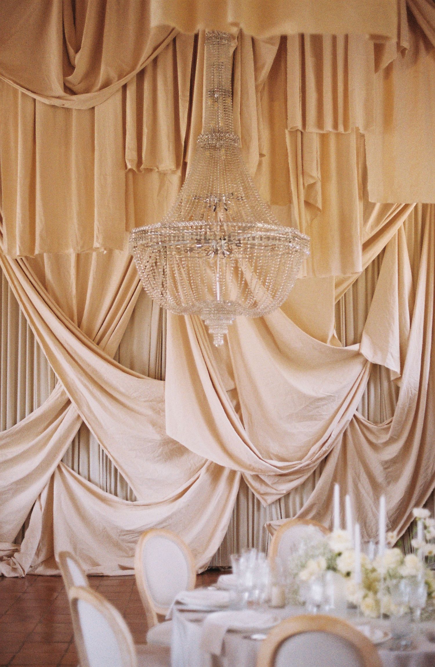 Elegant wedding reception decor features draped white fabric and crystal chandeliers creating a romantic ambiance.