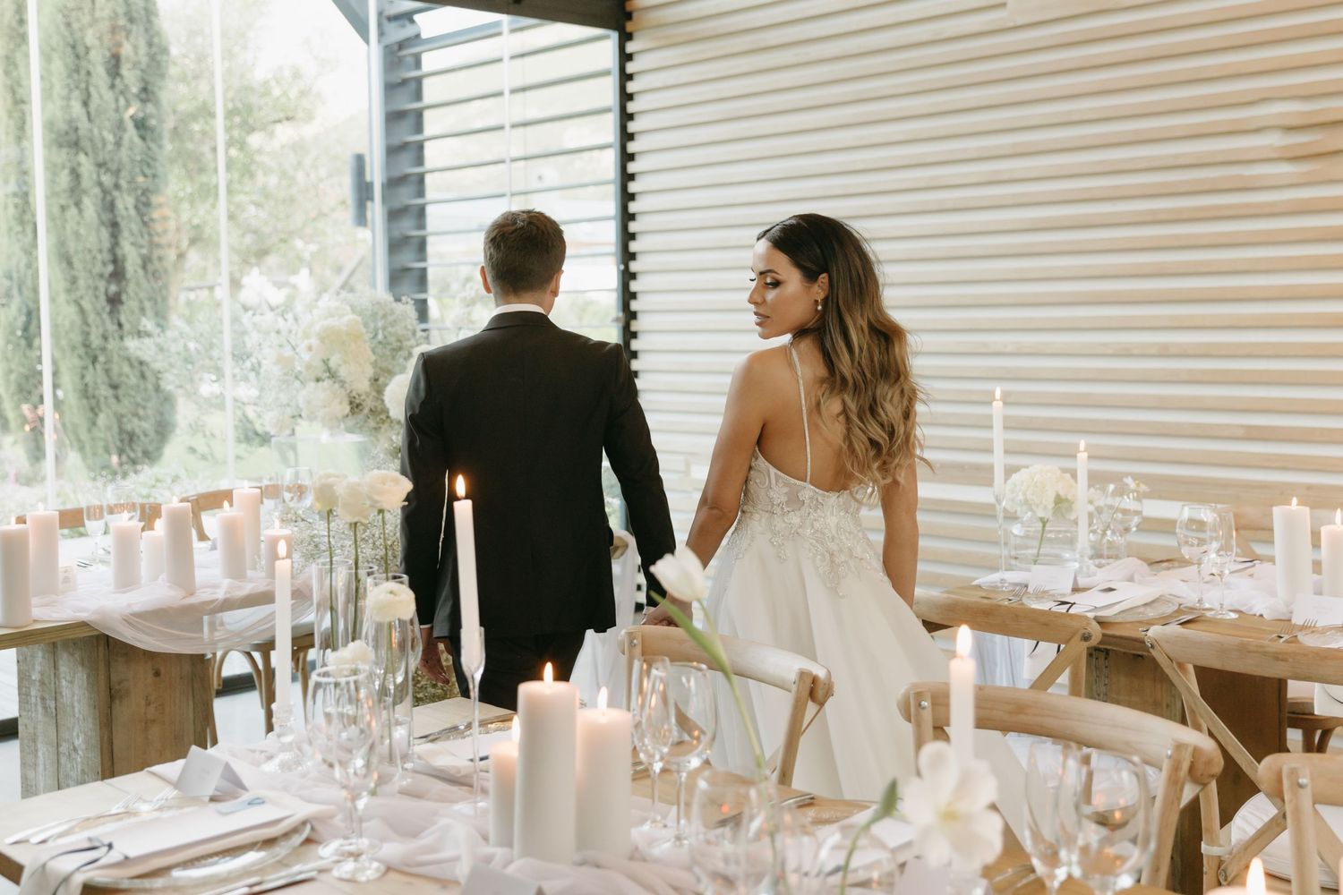 Bride and groom standing at elegant wedding reception table with white candles and floral decor.