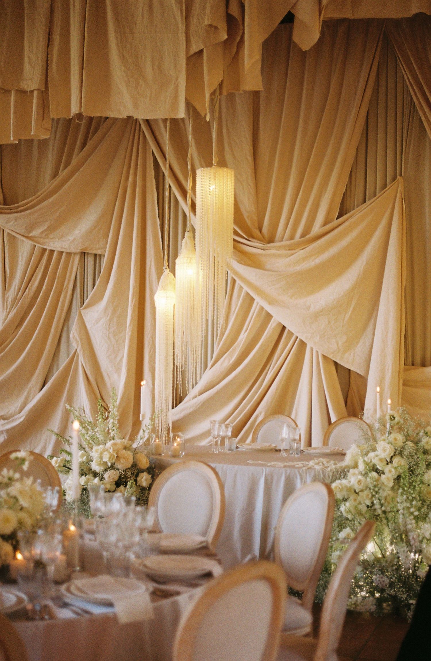 Elegant wedding reception venue with white draped fabric ceiling and floral centerpieces on dining tables.