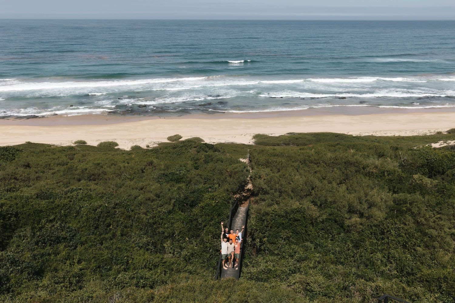 Panoramic view of a coastal landscape with rolling green hills meeting sandy beach and blue ocean waves.