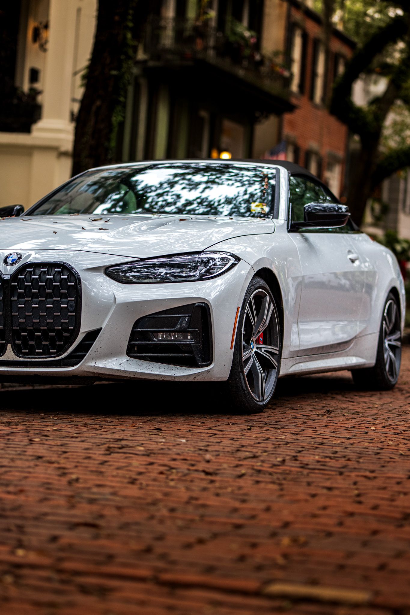 A sleek white BMW 4 Series with the distinctive large kidney grille parked on a brick street in an urban setting.