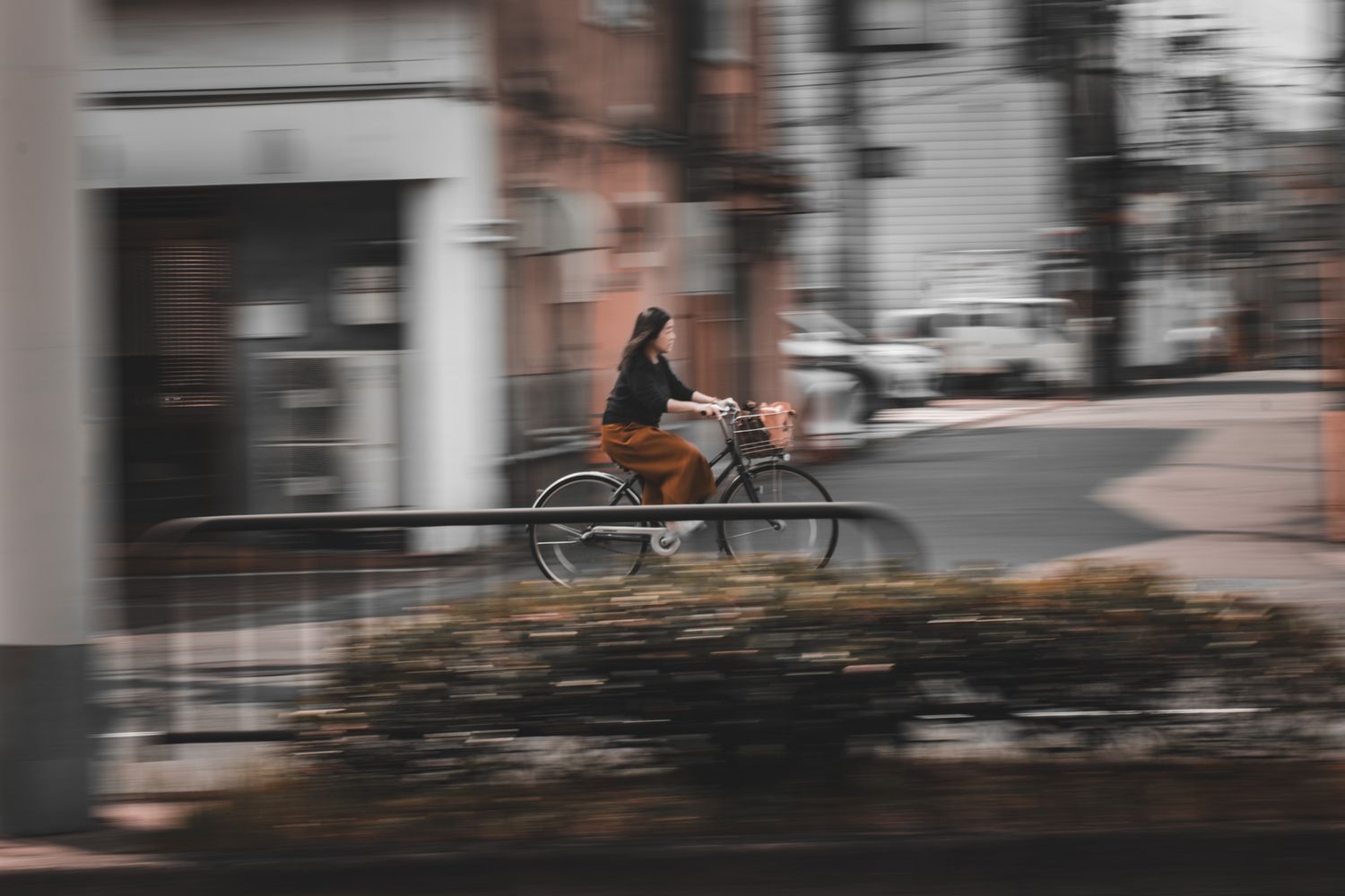 A cyclist rides through an urban street captured with motion blur panning technique on a vintage-style bicycle.