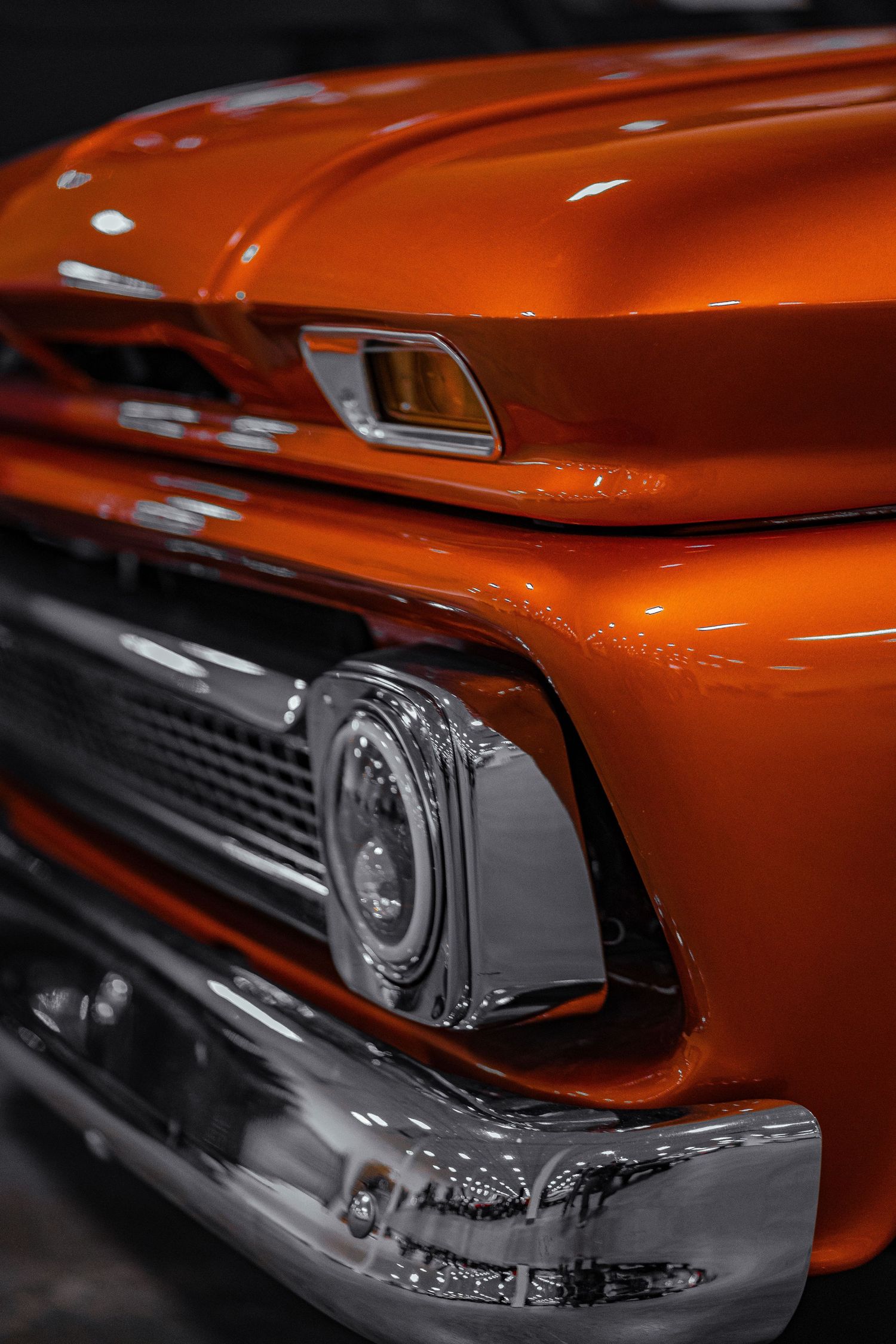 Orange vintage GMC truck front end showing chrome trim and headlight assembly.