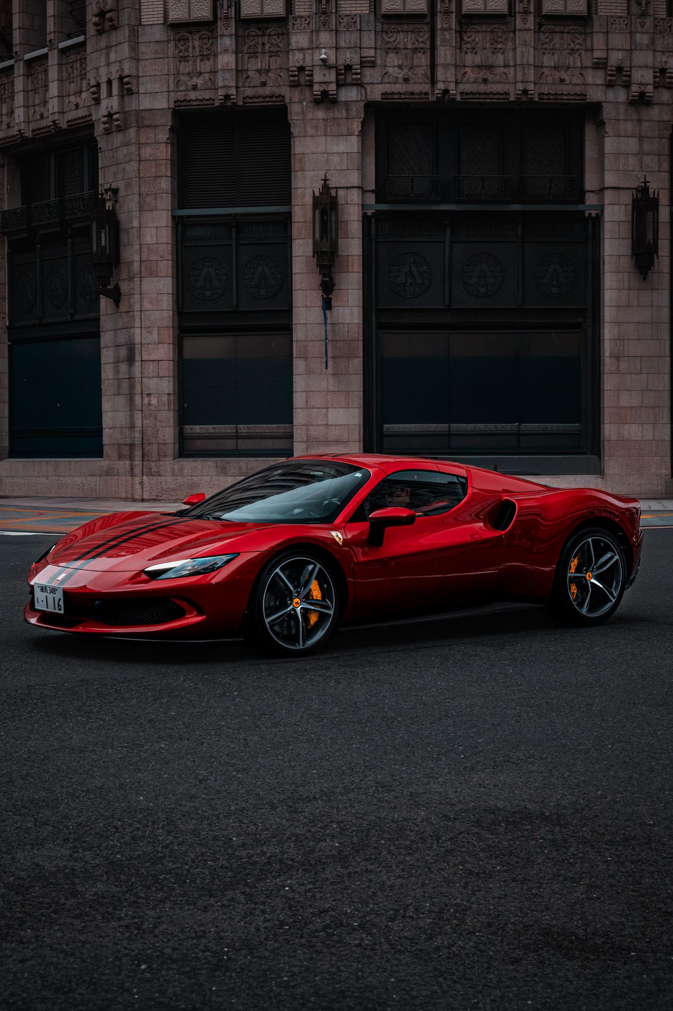 A stunning red Ferrari 296 GTB supercar parked on a city street in front of a classic stone building.