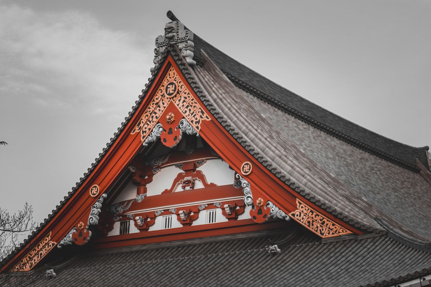 Ornate red and gold Japanese temple roof gable with intricate decorative carvings against a gray sky.