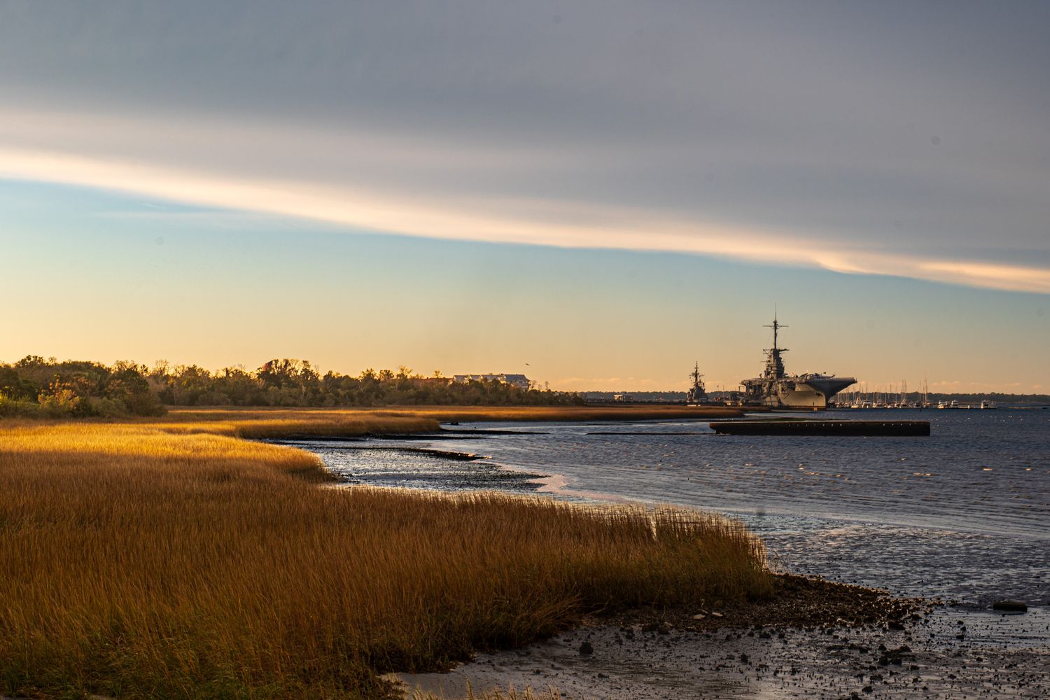 Golden marsh grass and calm waters at sunset with a distant ship silhouetted against the colorful horizon.
