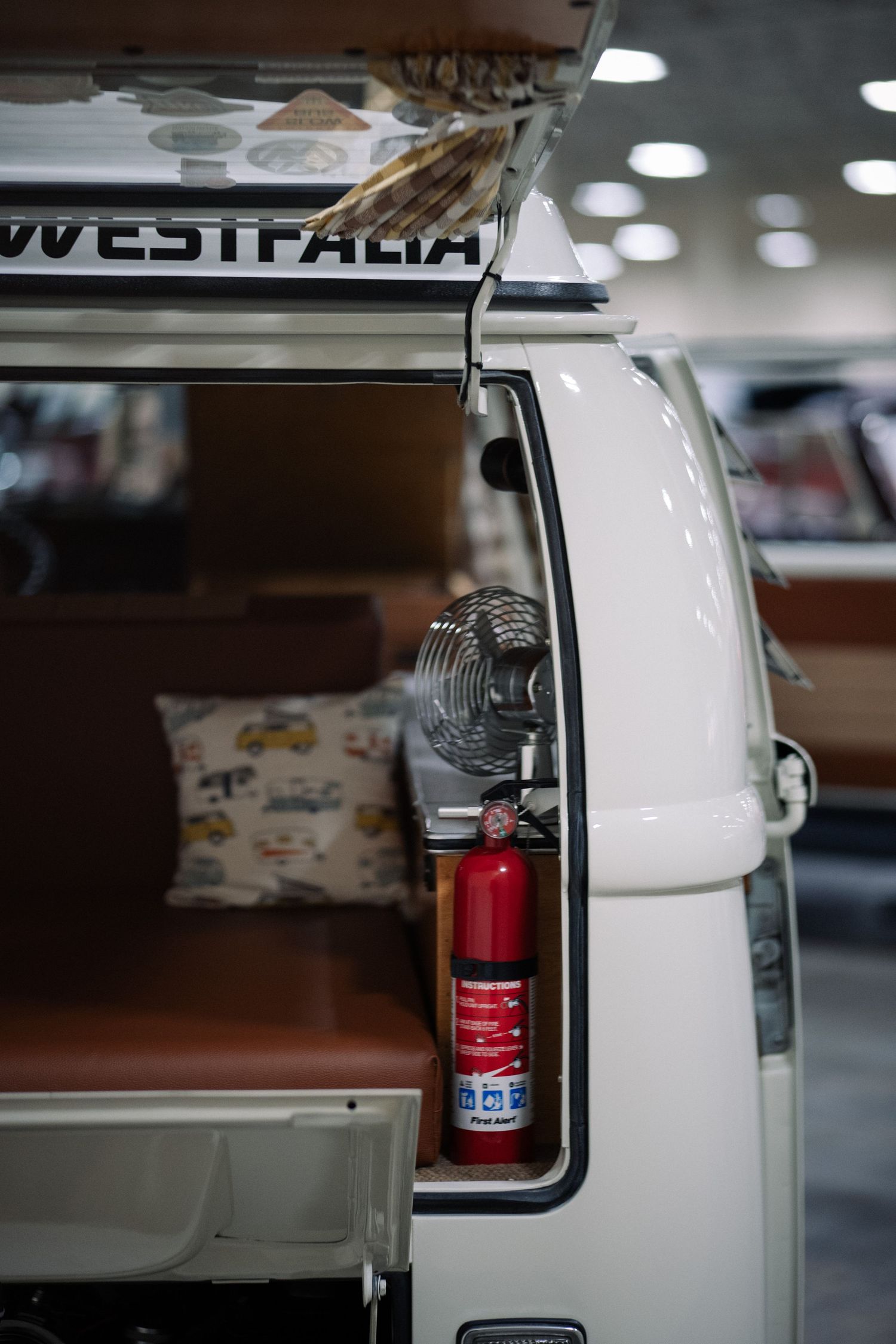 Vintage white car interior detail showing red fire extinguisher mounted inside the passenger compartment.