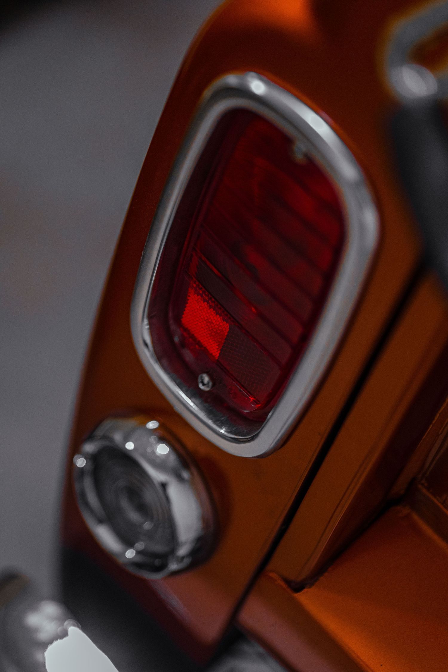 Close-up of vintage red taillight with chrome trim on orange vehicle.