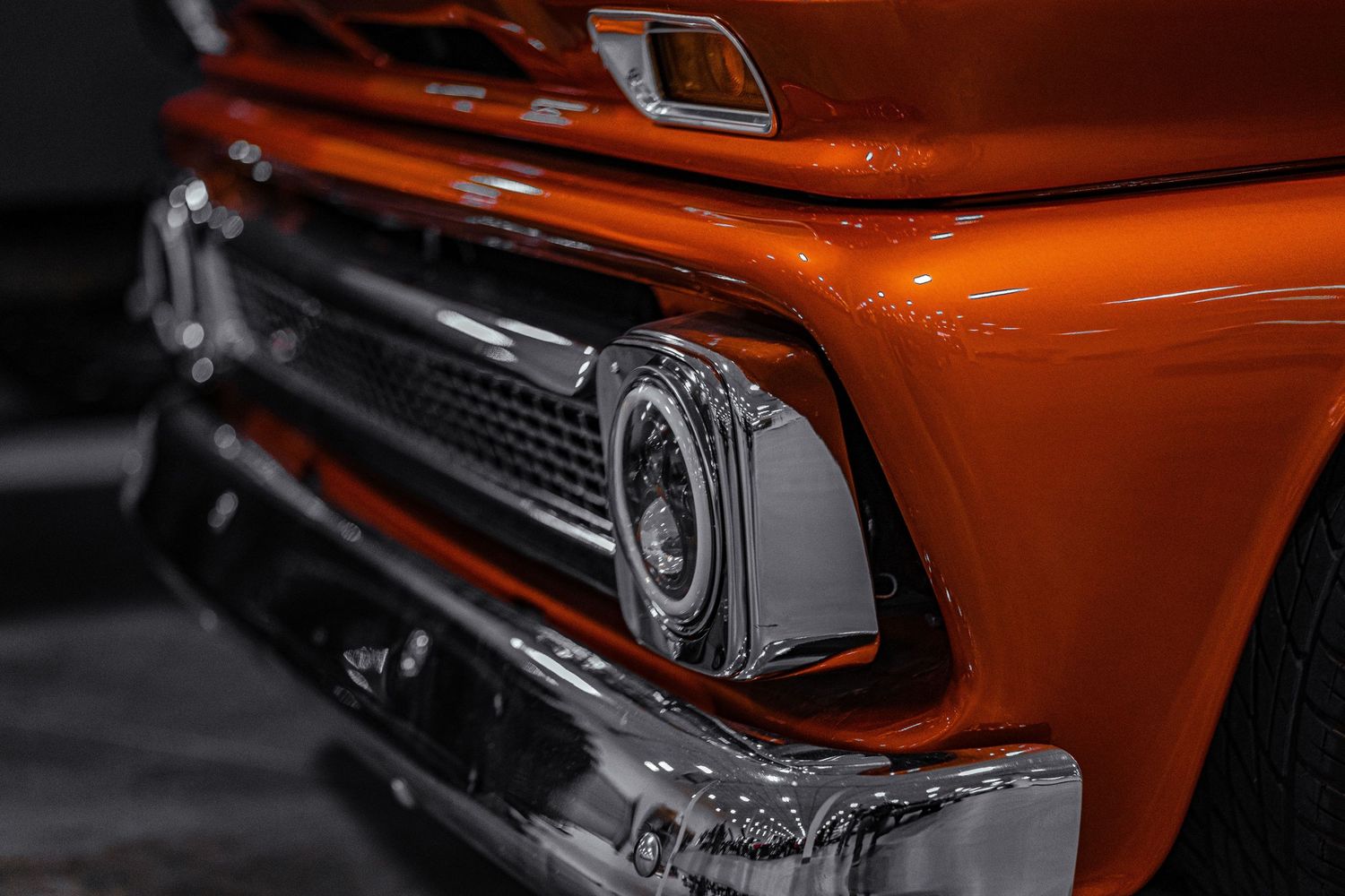 Front end detail of classic orange GMC truck showing chrome grille and headlight.