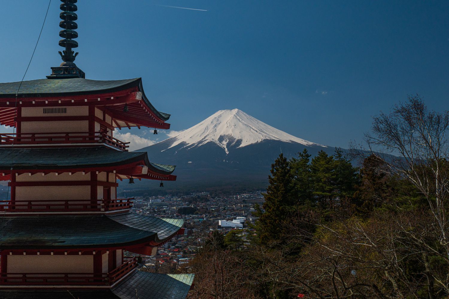 Red Japanese pagoda with Mount Fuji snow-capped peak rising behind it against a clear blue sky.