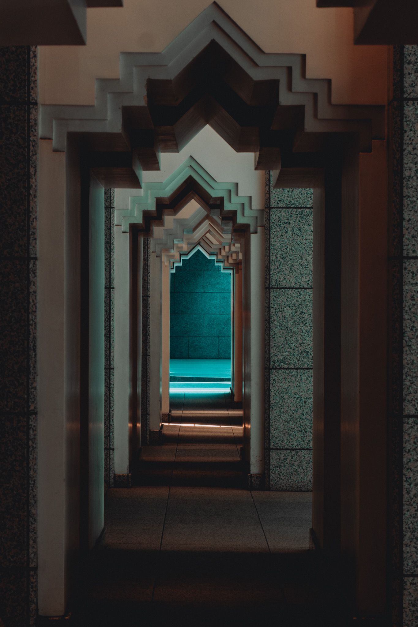 Ornate Islamic archway corridor with repeating pointed arches receding into a teal-lit interior.
