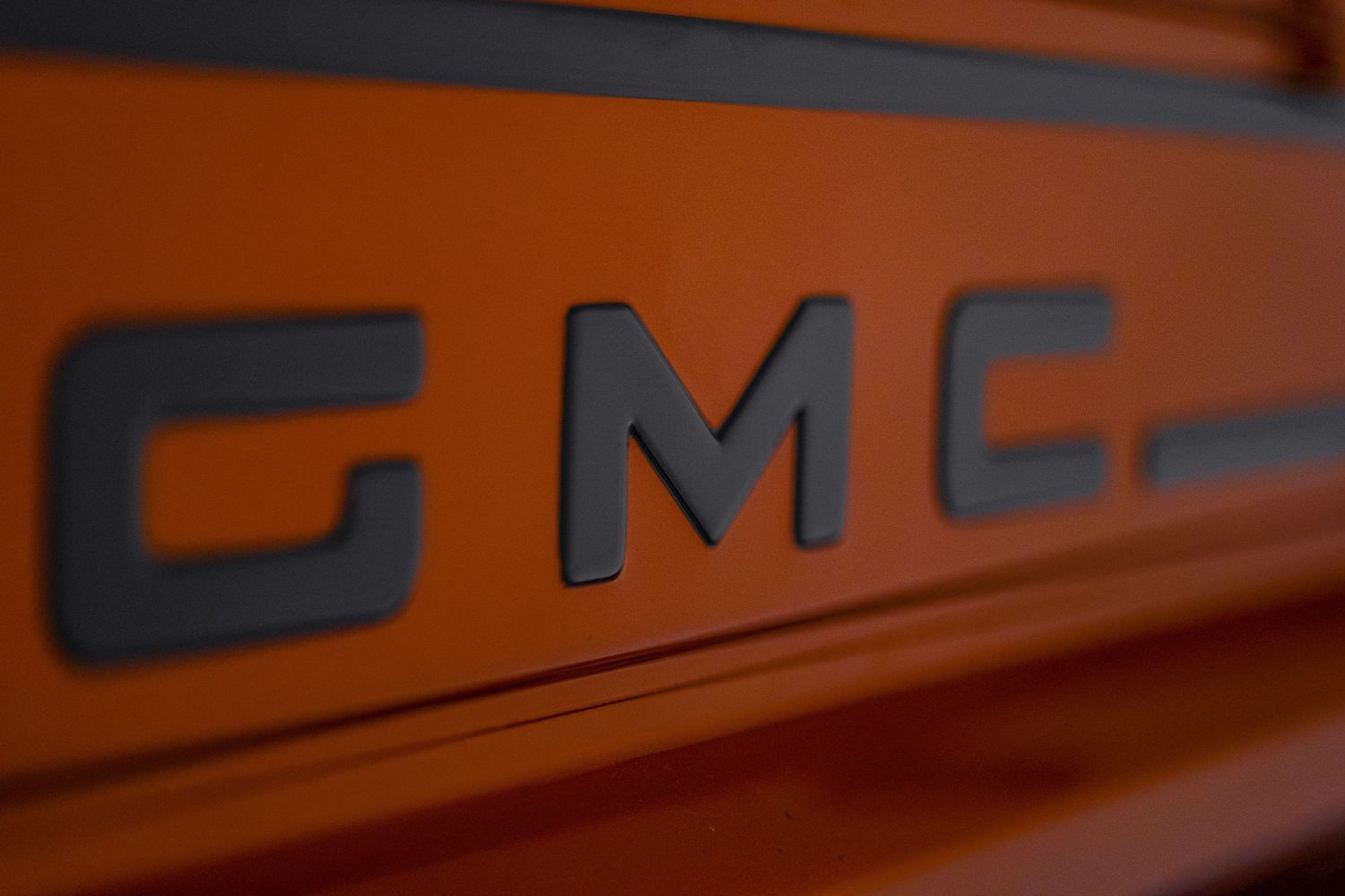 Macro shot of black GMC lettering on orange painted surface.