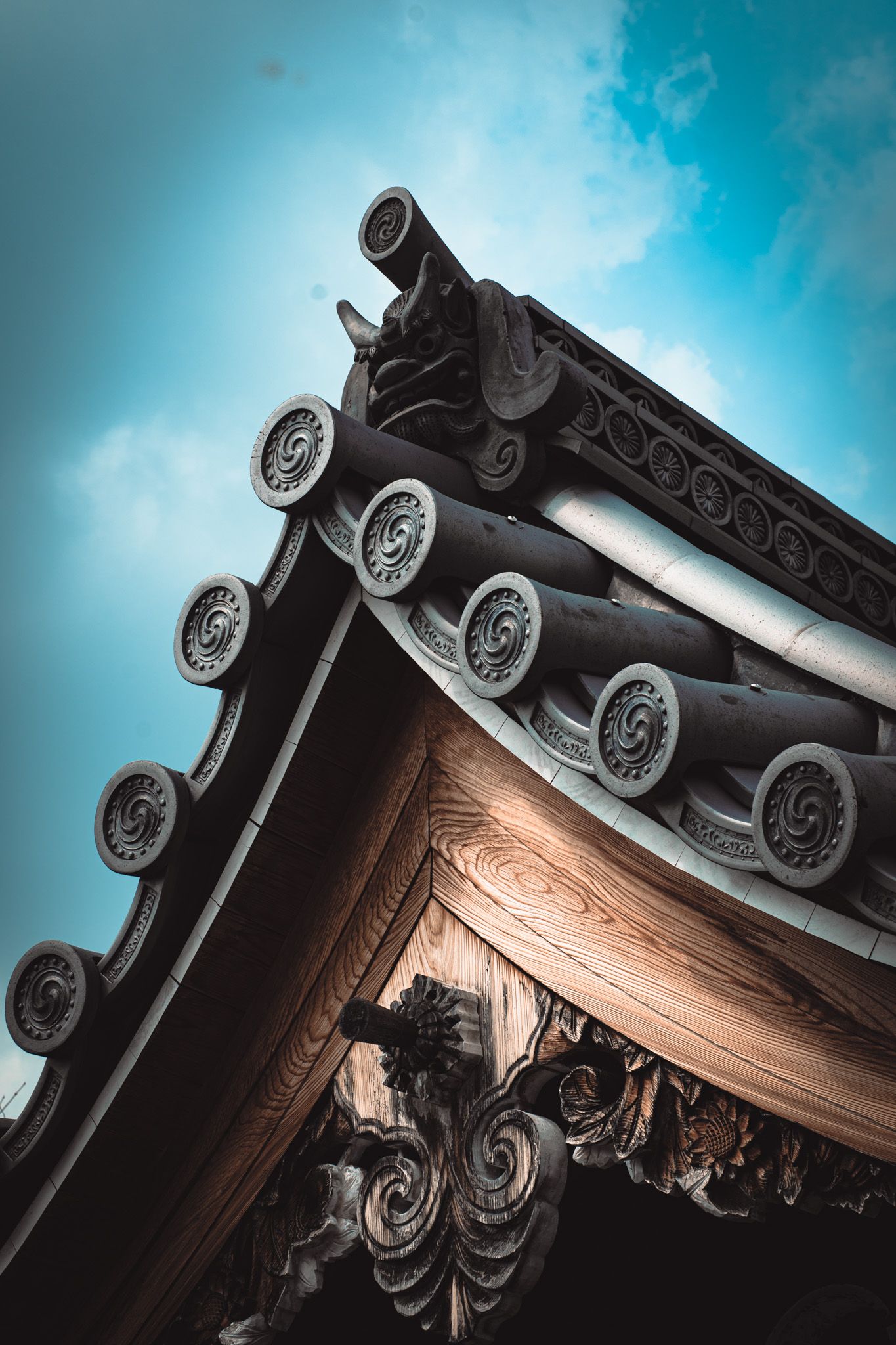 Close-up of ornate Japanese temple roof eave with decorative circular tile ends against a blue sky.